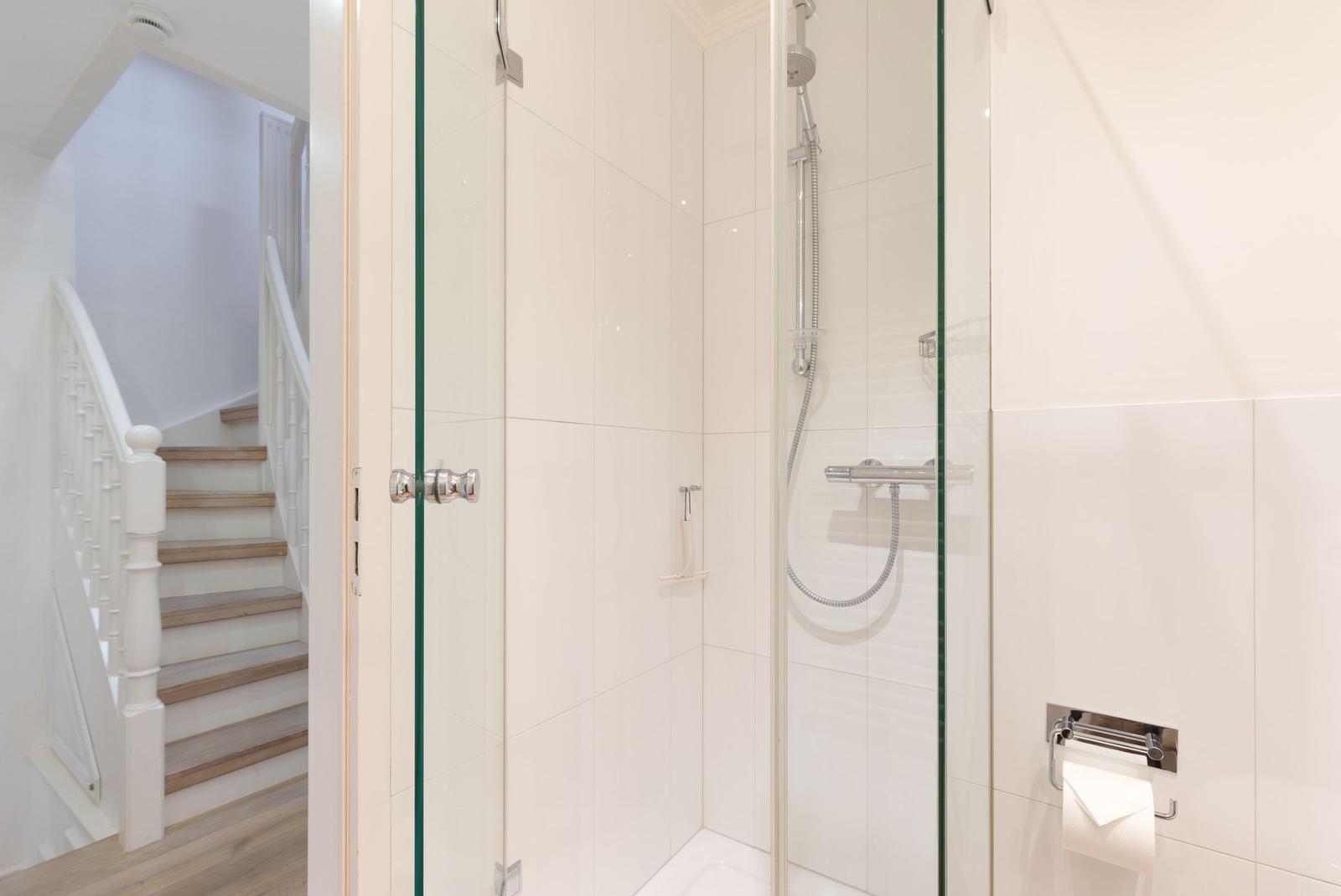 Duschkabine mit Glaswand und Toilettenpapierhalter. Treppenhaus im Hintergrund.