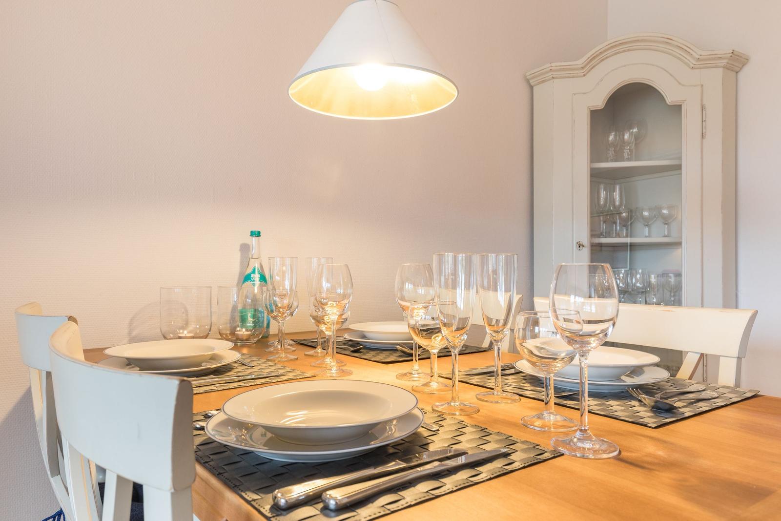 Esszimmer mit gedecktem Tisch, weißen Stühlen und Glasvitrine.