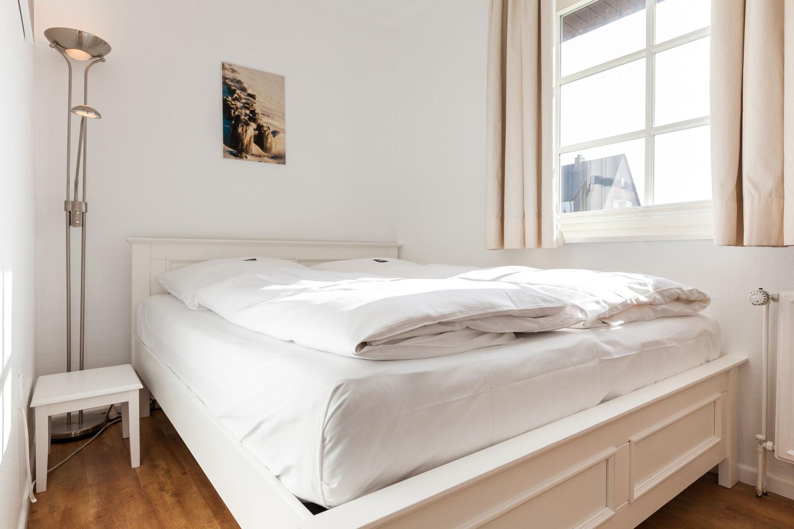 Schlafzimmer mit weißem Bett, Fenster und Stehlampe.