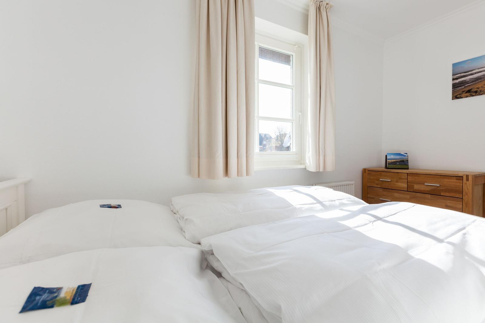 Schlafzimmer mit Doppelbett, Fenster und Holzschrank.