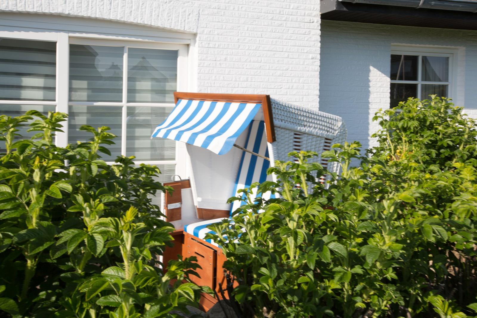 Blau-weiße Strandkörbe stehen im Garten vor einem weißen Haus.