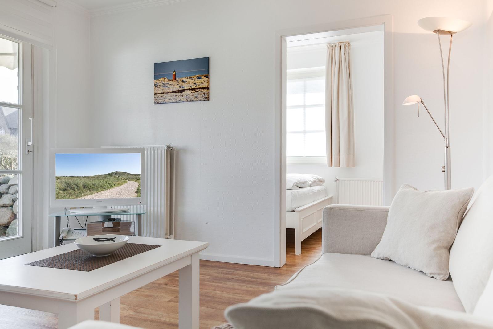 Wohnzimmer mit Sofa, Fernseher und Blick in Schlafzimmer