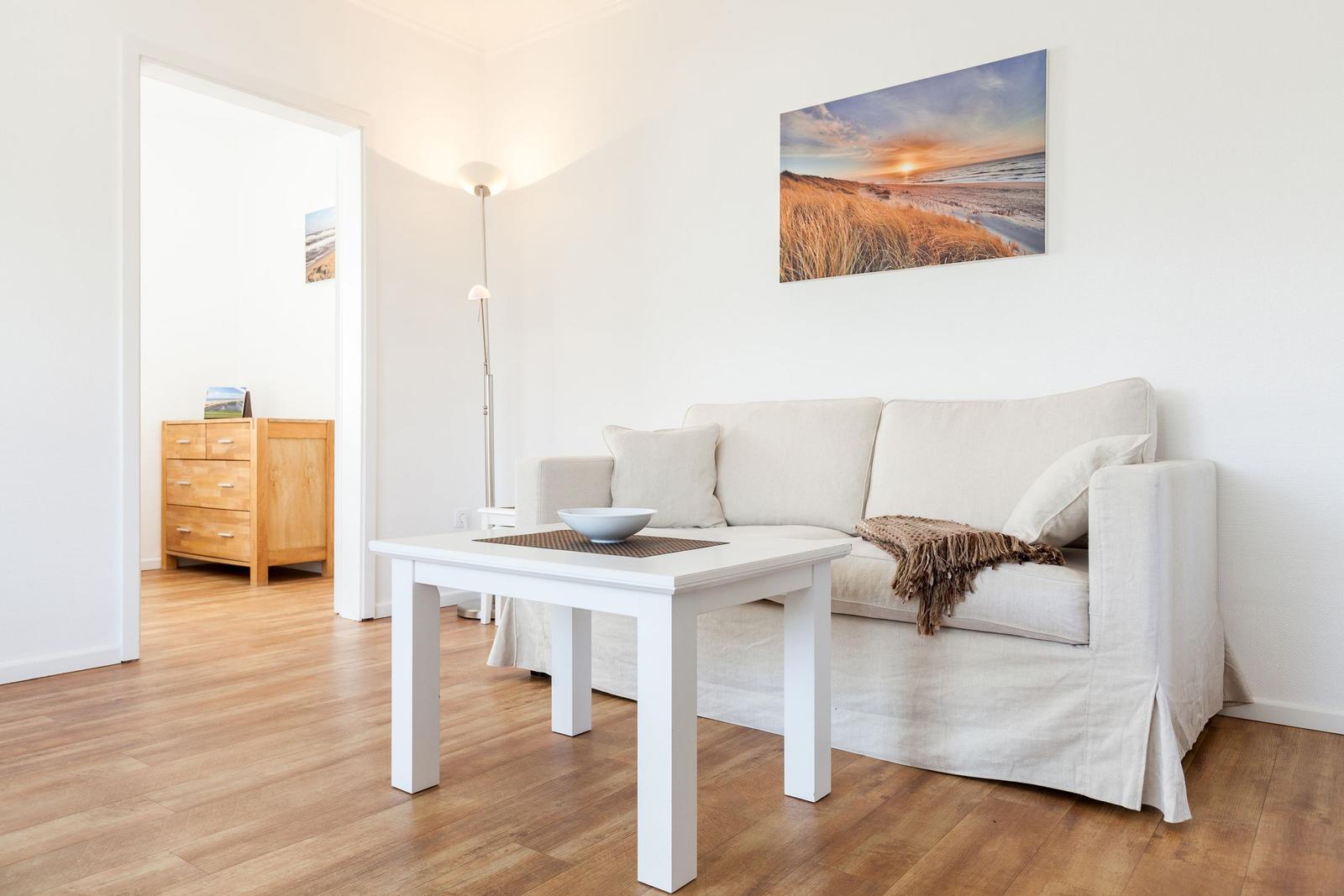 Wohnzimmer mit Sofa, Tisch und Wandbild. Holzfußboden und weiße Wände.