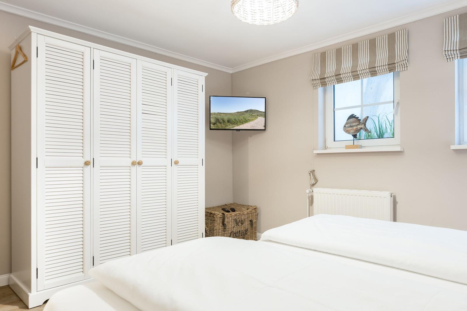 Bedroom with white bed, wardrobe, and TV on the wall.