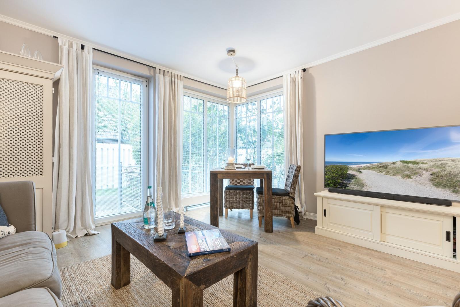 Living and dining area with large windows, TV, and wooden table.