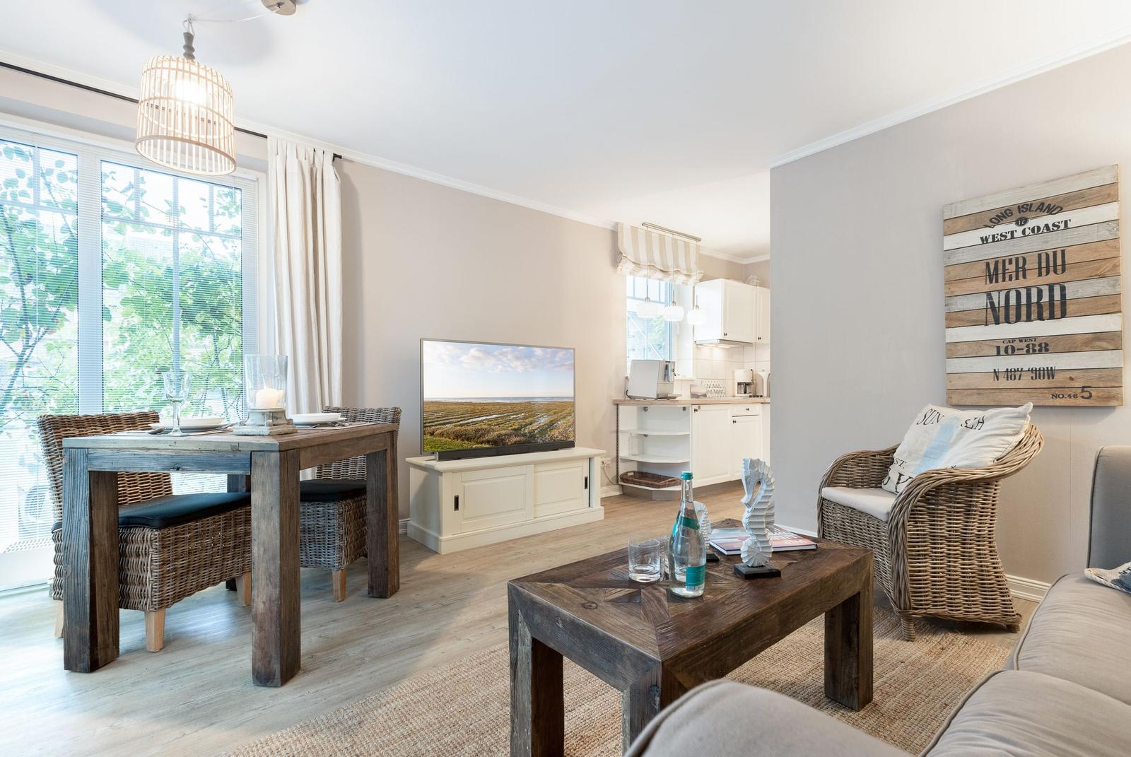 Living room with dining table, TV, and kitchen area. Wooden furniture and wall decor.