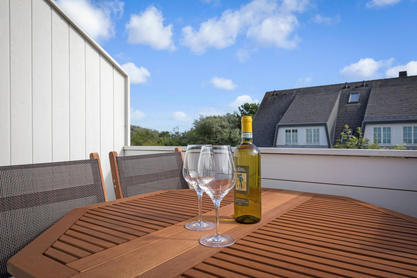 Terrasse mit Tisch, Stühlen und Weinglas. Hintergrund: Haus und Himmel.