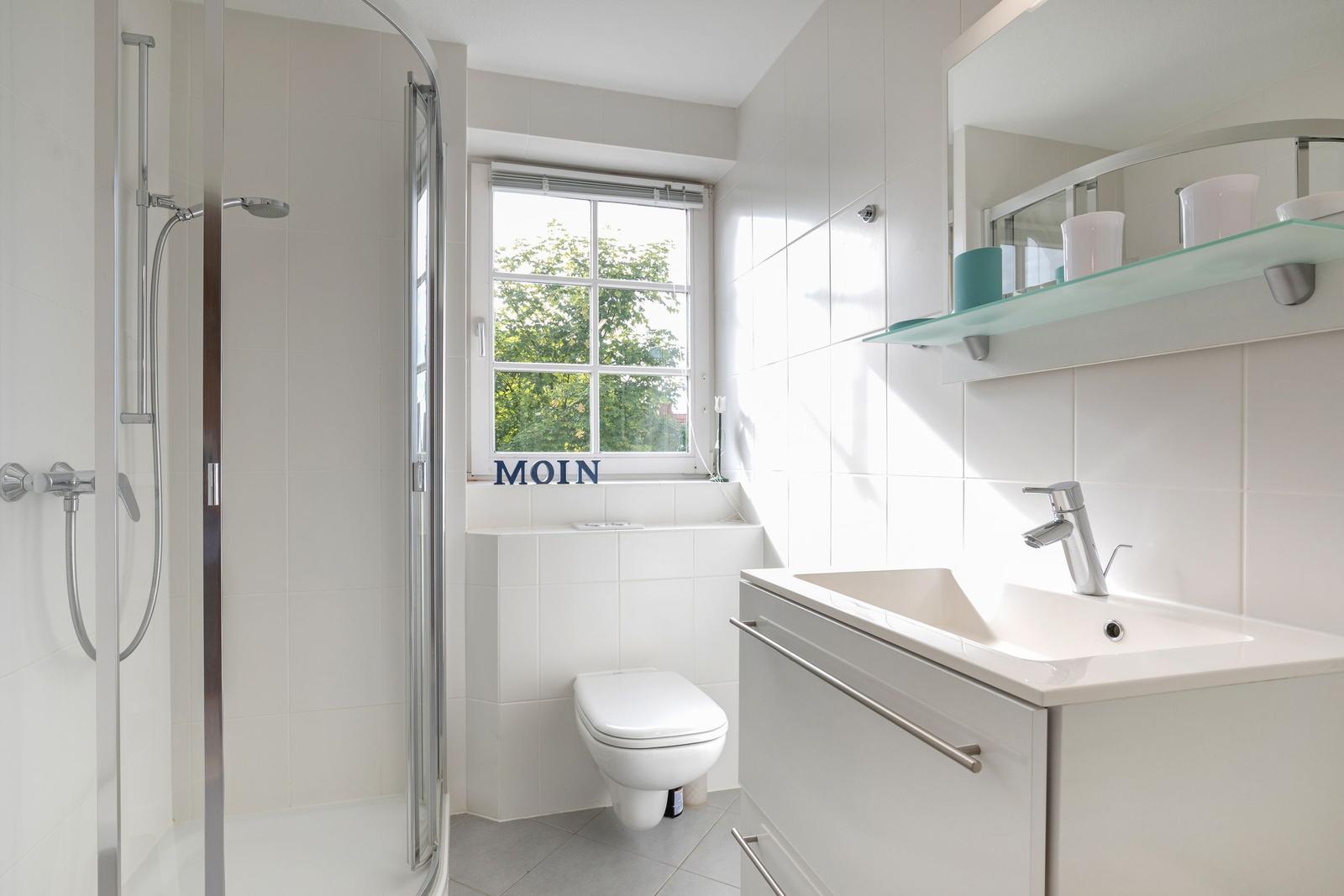 Badezimmer mit Dusche, Waschbecken und Toilette. Fenster mit Blick auf Grün.