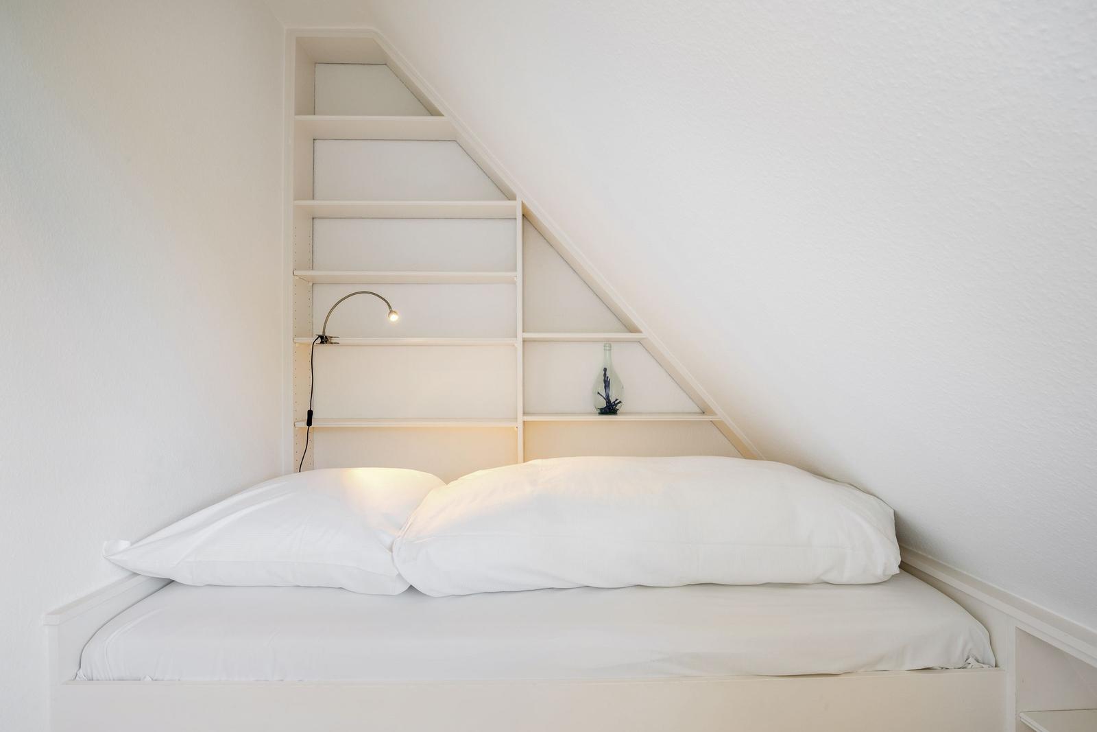 Schlafzimmer mit Dachschrägen, Bett und Regalwand.
