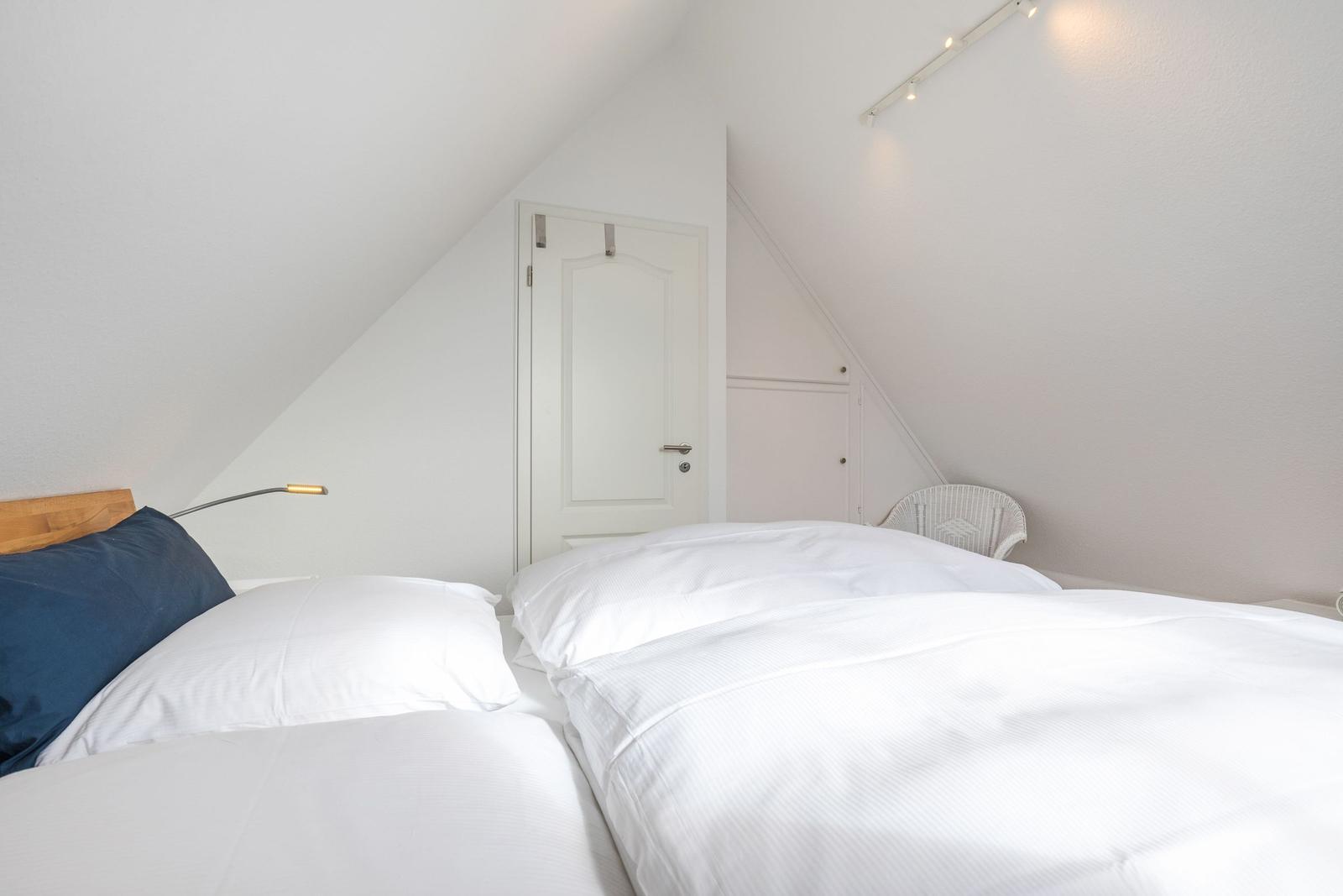 Schlafzimmer mit Doppelbett, weißer Wand und Tür unter Dachschrägen.