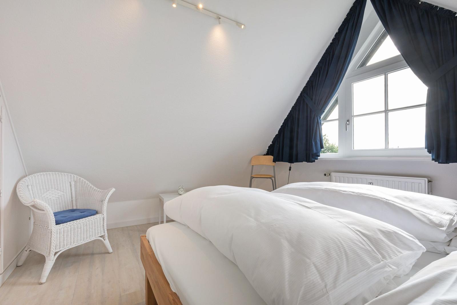 Schlafzimmer mit Doppelbett, weißen Wänden und großem Fenster mit dunkelblauen Vorhängen.