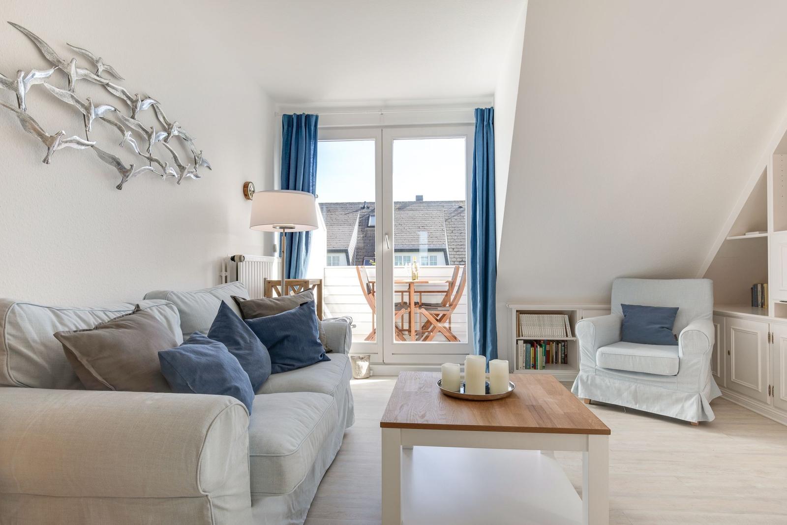 Wohnzimmer mit Sofa, Sessel und Balkonansicht.