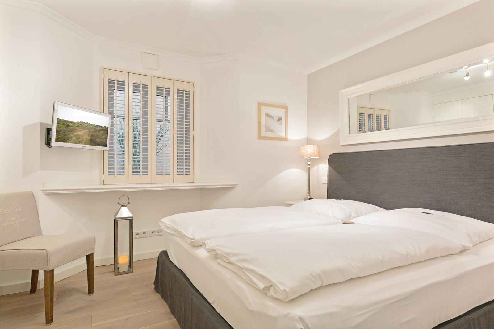 Schlafzimmer mit Bett, Fernseher und Fenster mit Jalousien.