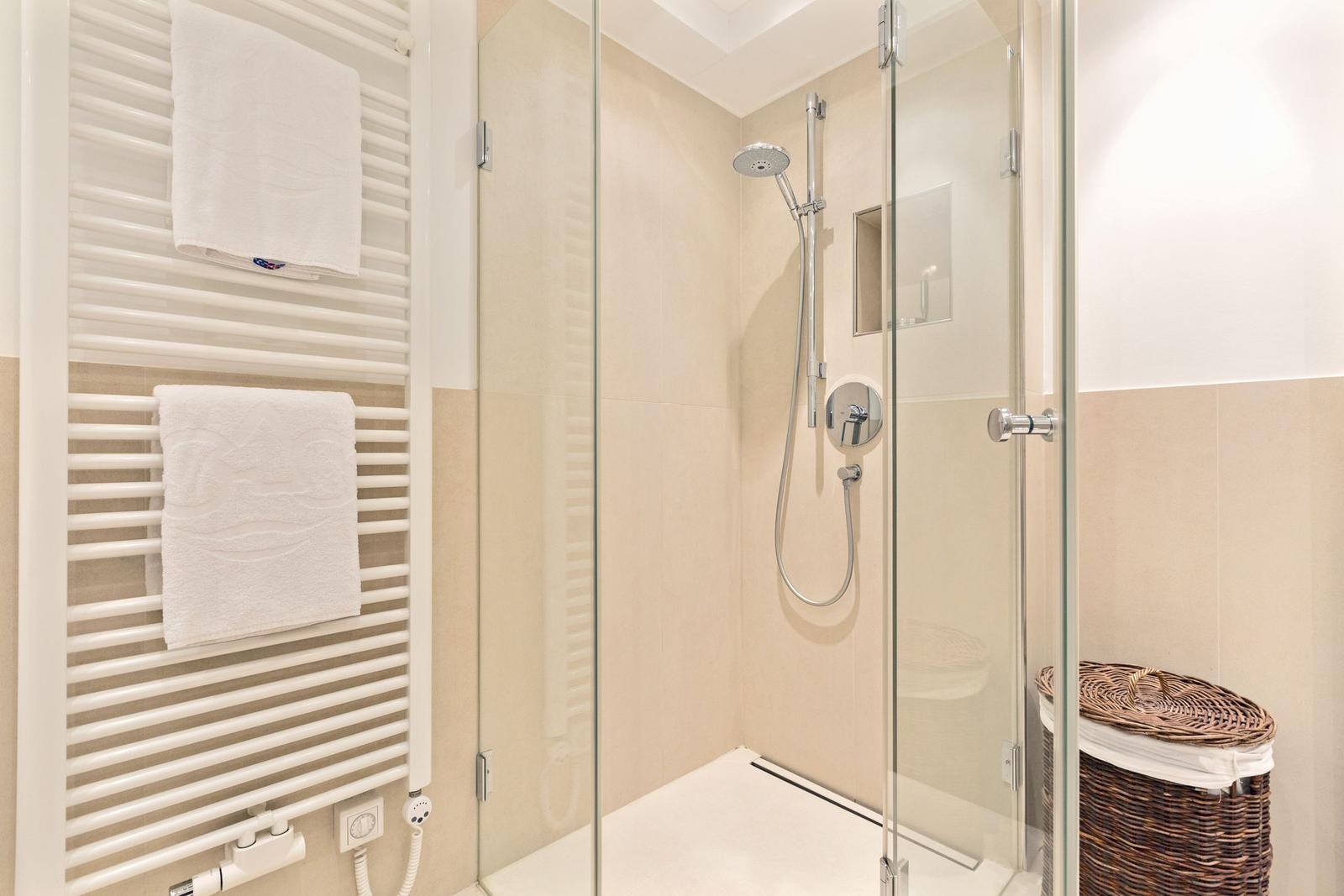 Dusche mit Glaswand, Handbrause und Heizkörper mit Handtüchern.