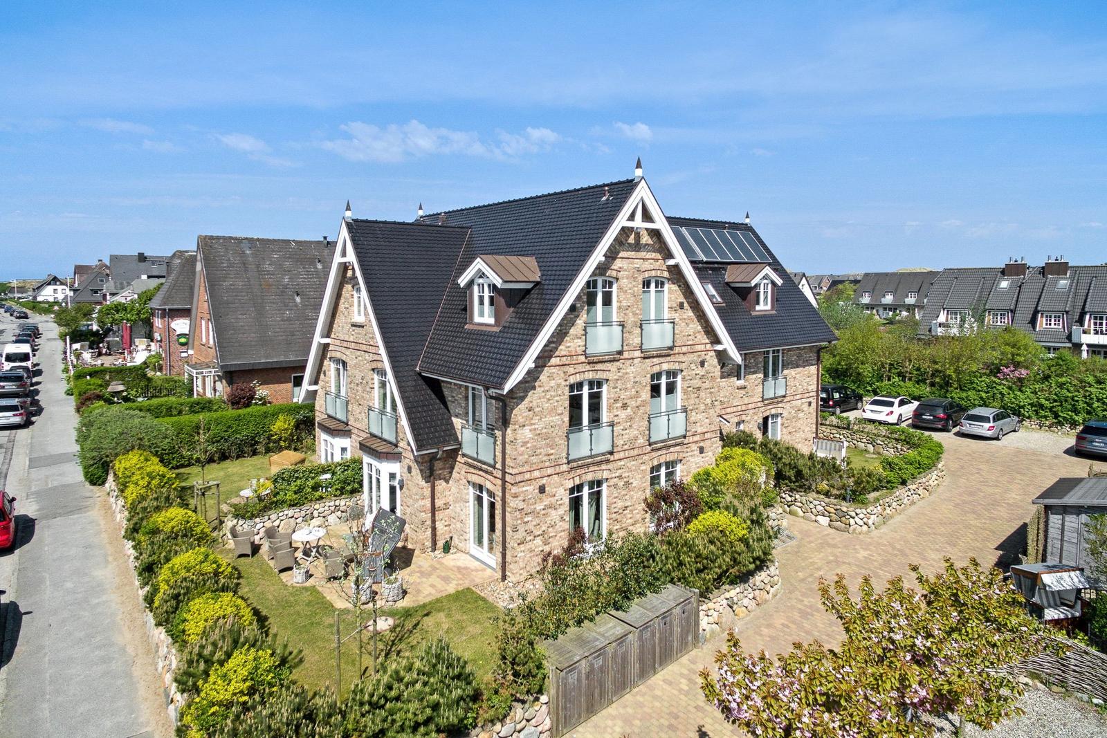 Ein zweistöckiges Steinhaus mit Balkonen und Garten. Mehrere Autos stehen auf dem Hof.