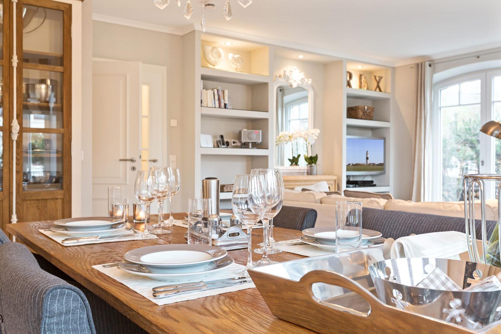 Esstisch mit Geschirr und Gläsern im Essbereich mit Wohnzimmer im Hintergrund.