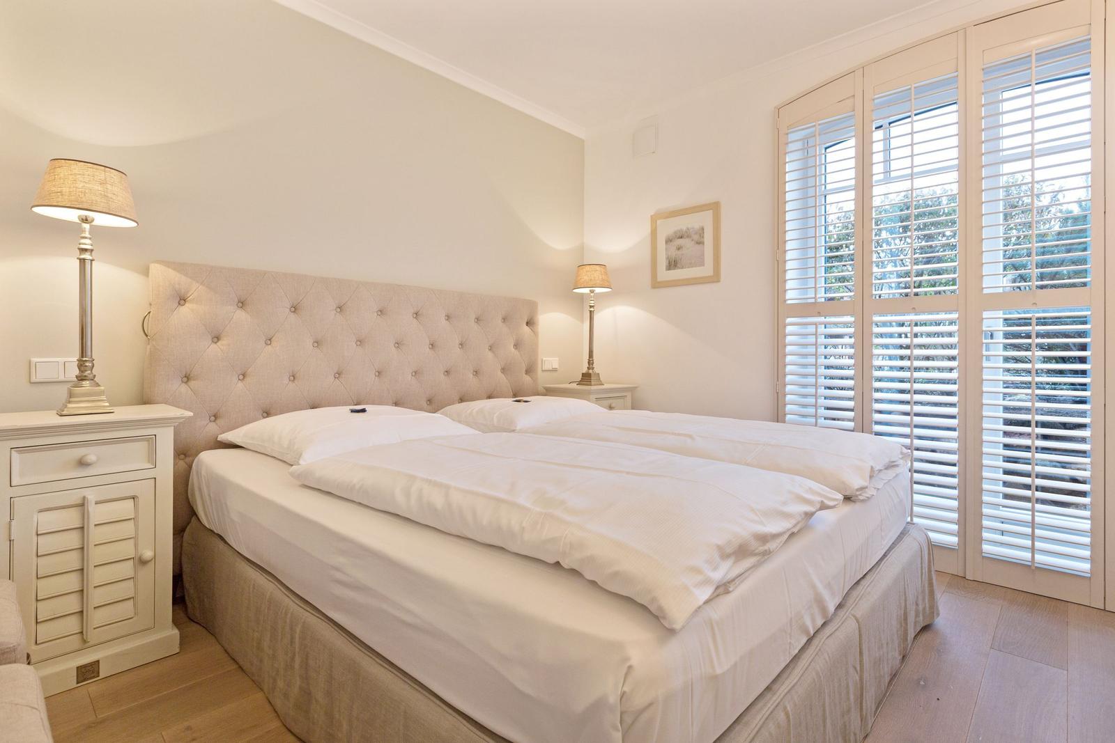 Schlafzimmer mit Doppelbett, zwei Nachttischen und Fenster mit Jalousien.