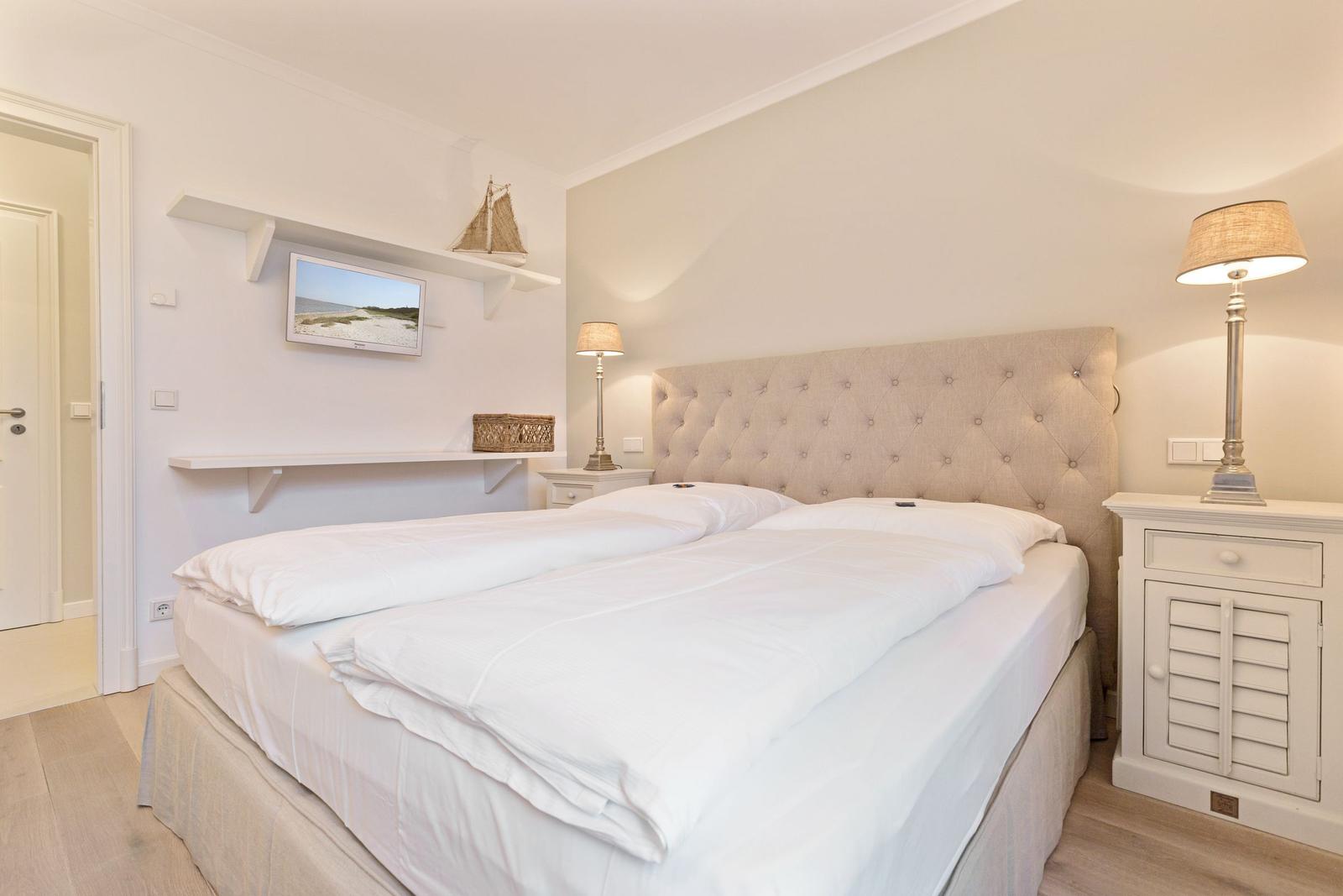 Schlafzimmer mit Doppelbett, Nachttisch und Wand-TV.