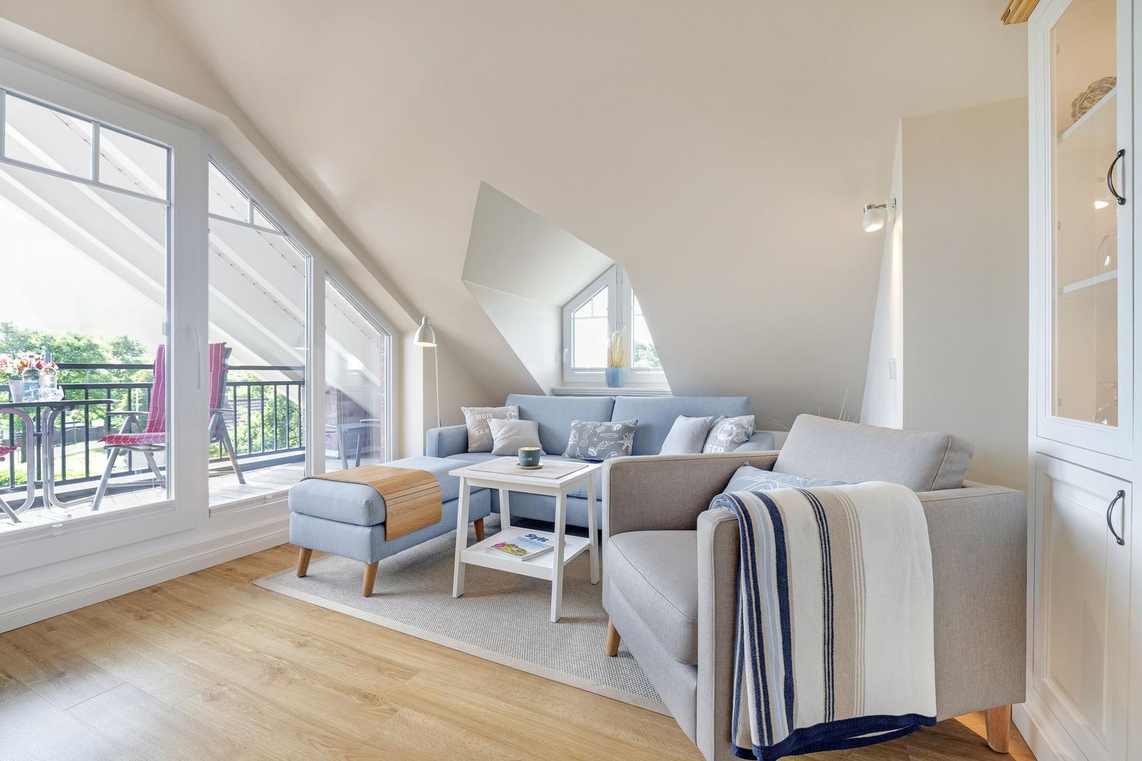 Living room with sofa, armchair, and balcony. Wooden floor and sloped ceiling.