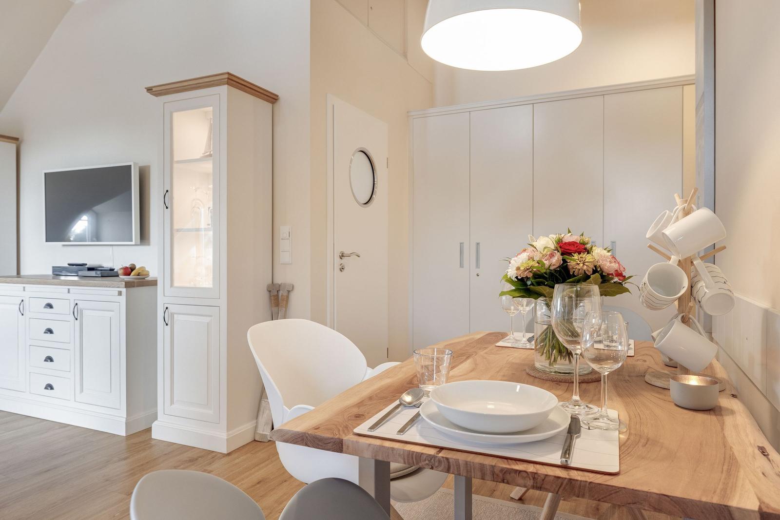 Dining area with wooden table, white chairs, and flower vase.