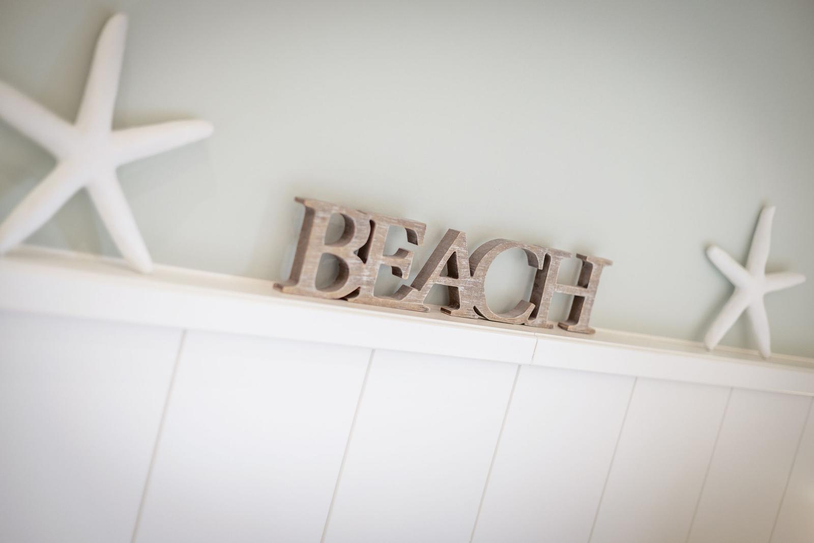 Wooden sign reading BEACH and two white starfish on a white panel wall.