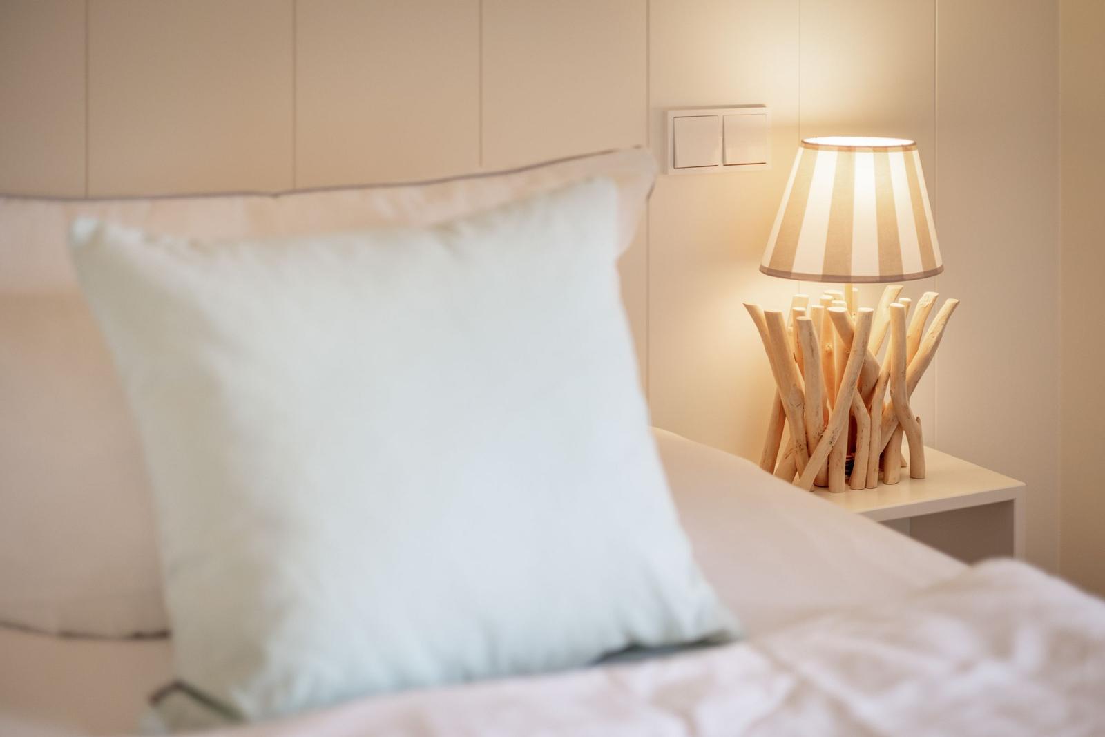 A bed with pillows and a bedside lamp with a wooden base.
