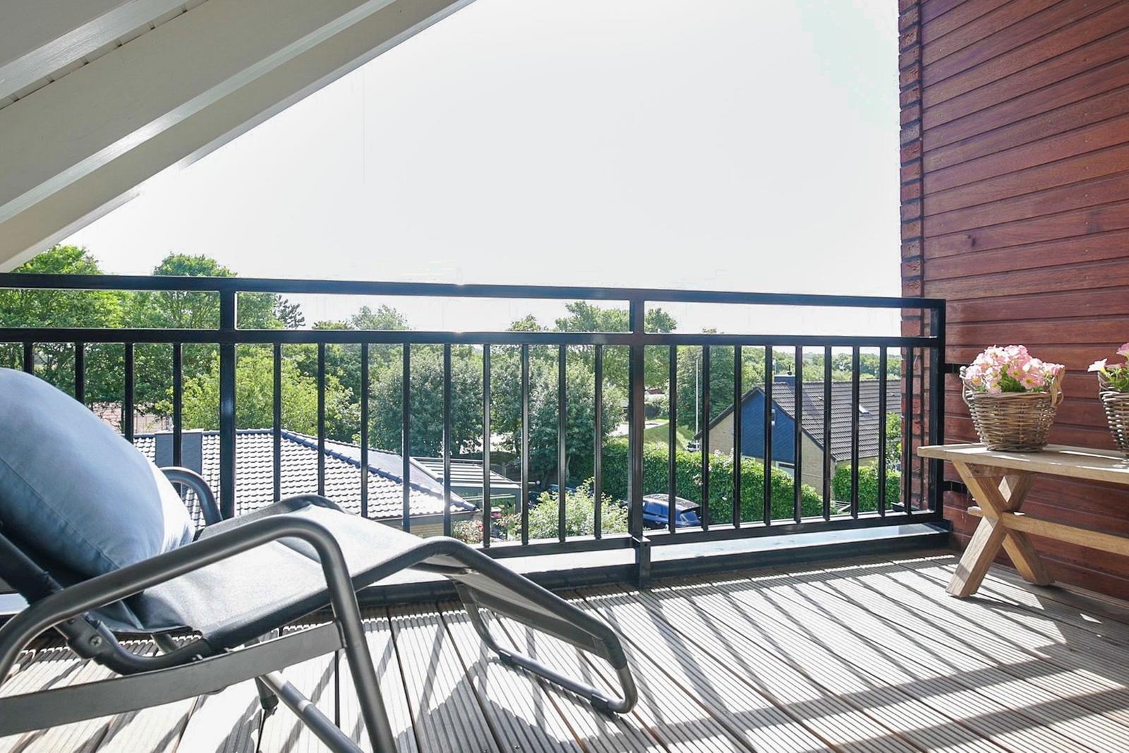 Terrace with lounge chair and flower basket. View of green surroundings and rooftops.