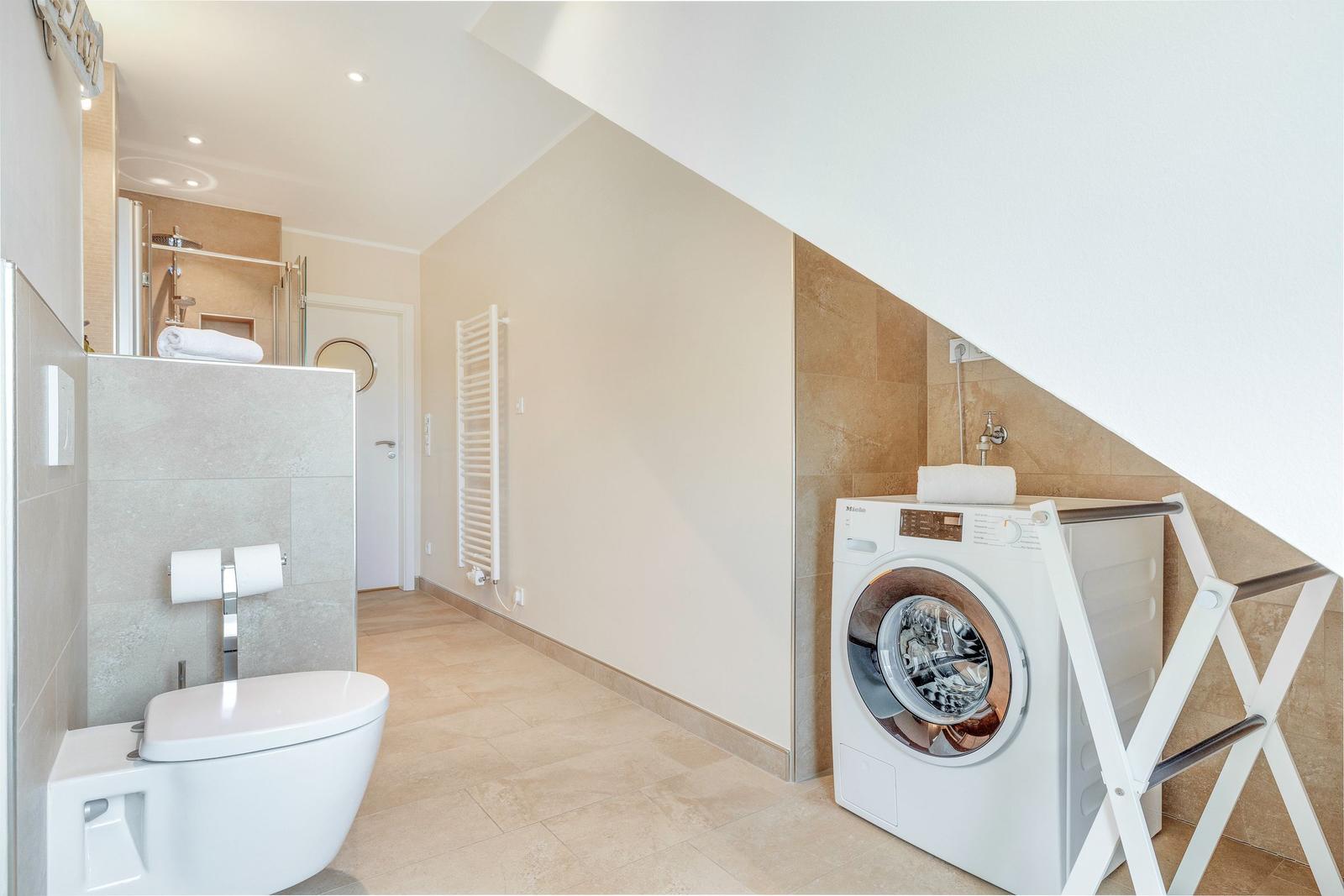 Bathroom with washing machine and toilet under sloped ceiling