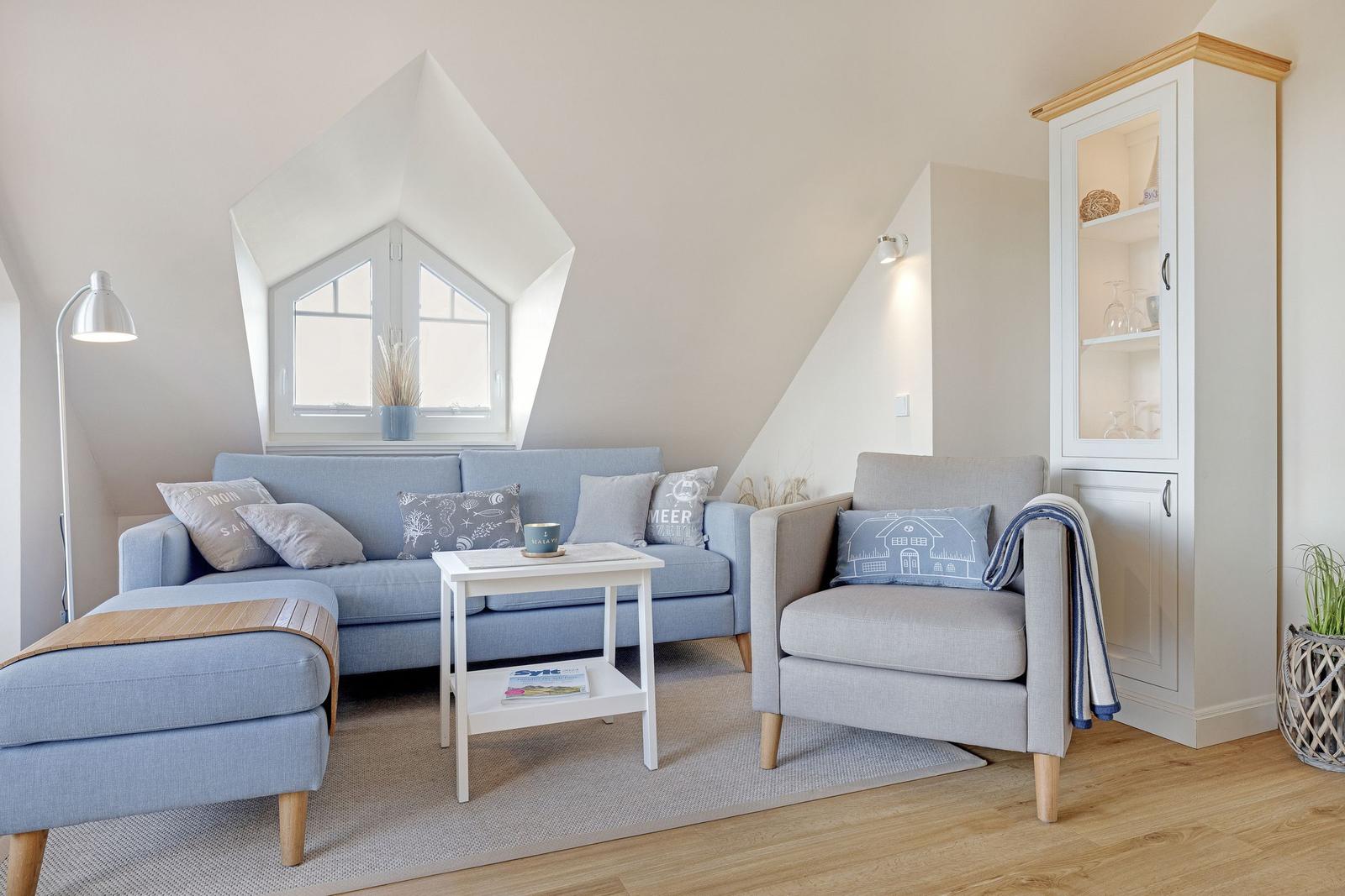 A living room with blue sofa, gray armchair and wooden floor. Against the wall is a cabinet with glass doors.
