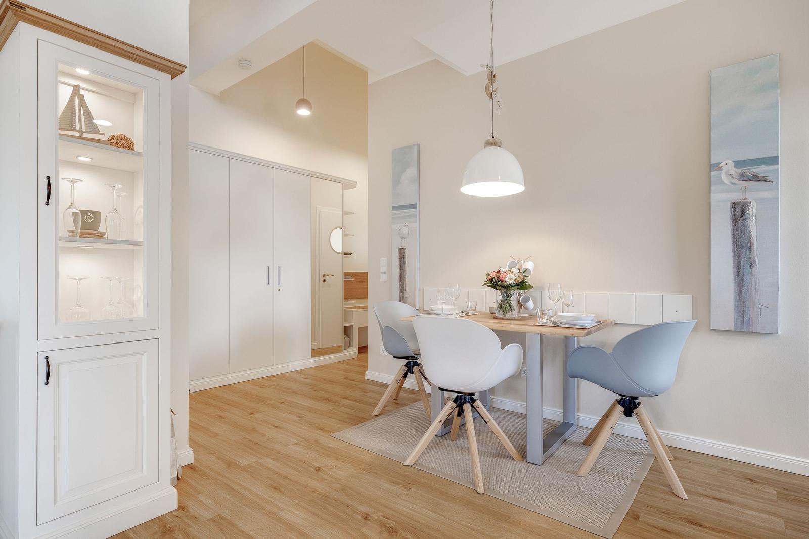 Dining area with table, chairs, and wall art. Wooden floor and white cabinet.