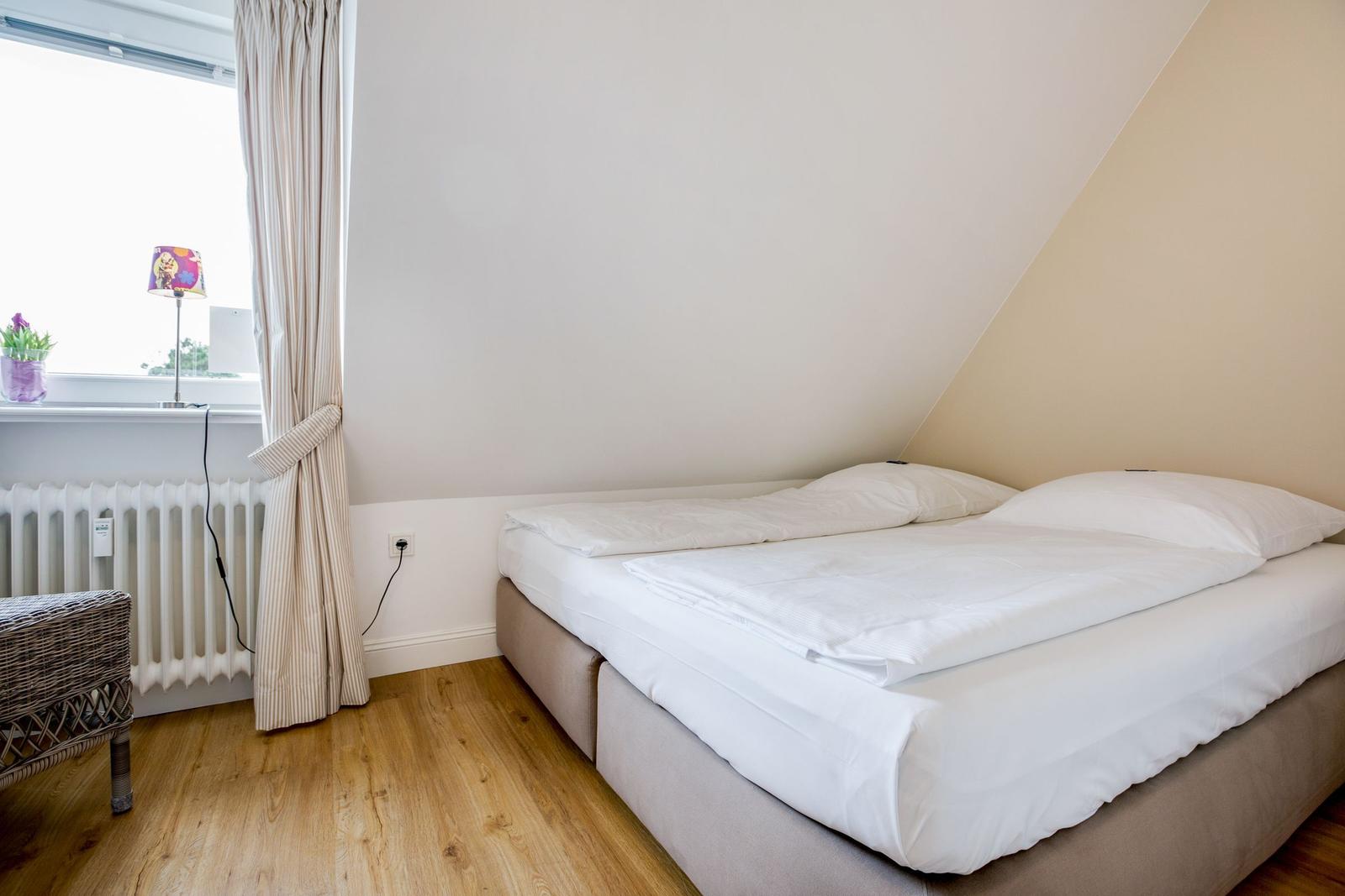 Schlafzimmer mit Doppelbett, Holzboden und Fenster mit Vorhang.