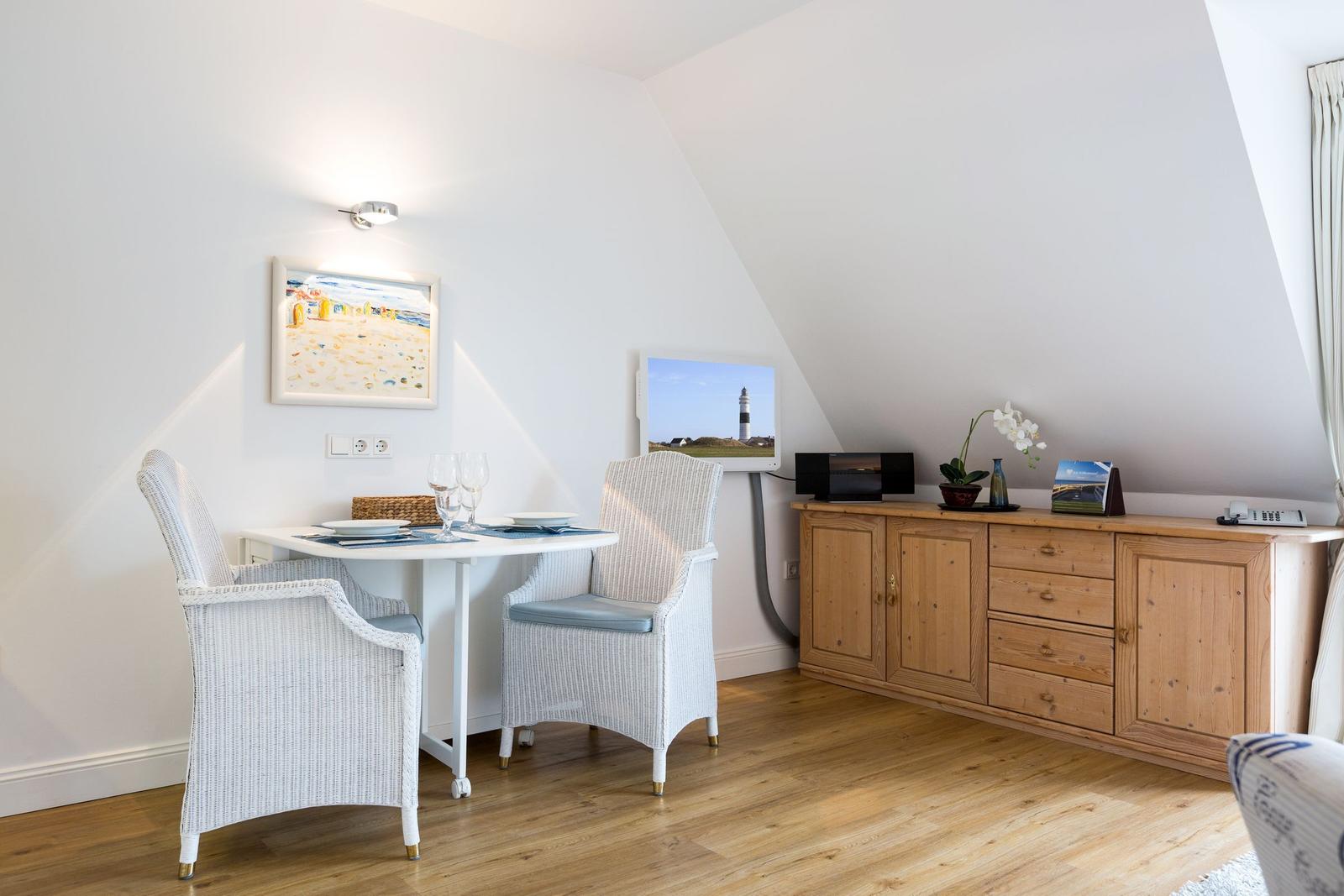 Essbereich mit Tisch, zwei Stühlen und Holzschrank an geneigter Wand.