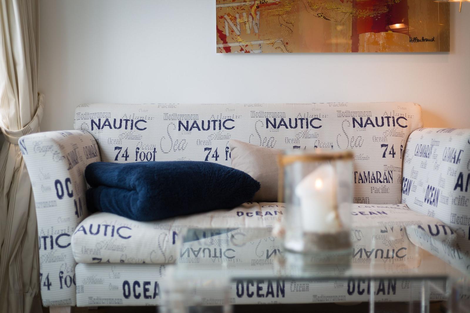 Sofa mit nautischem Muster, Kissen und brennender Kerze.