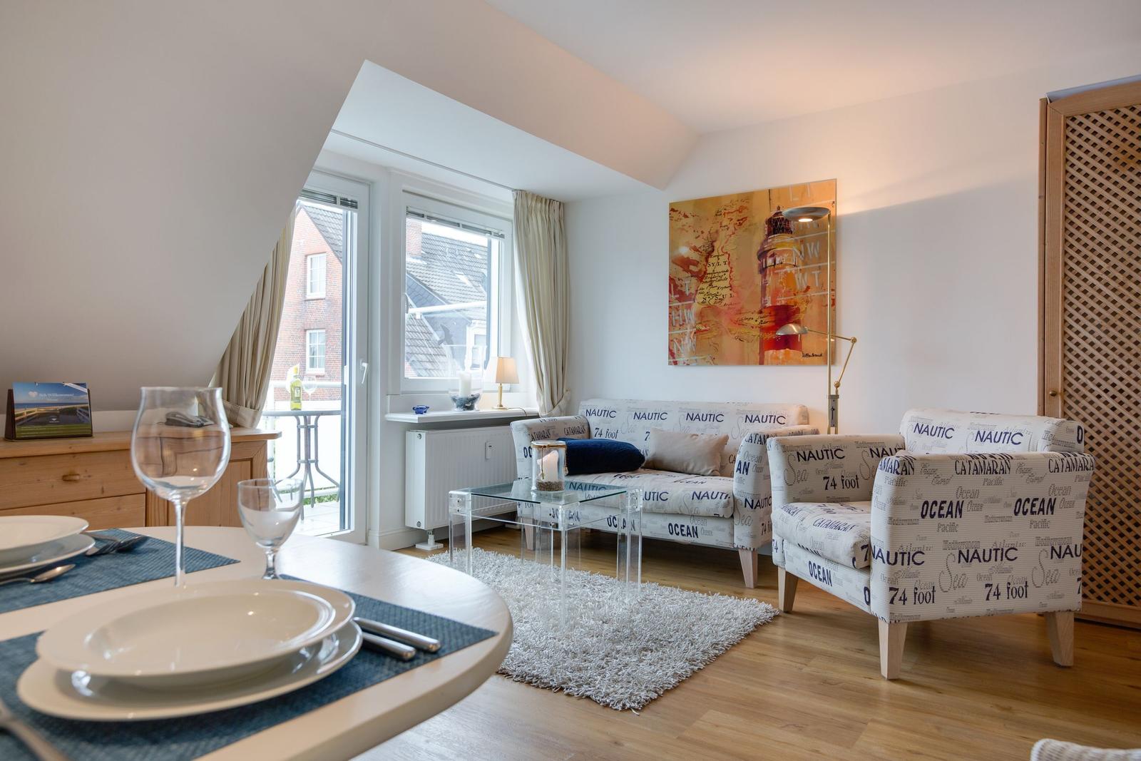 Wohn- und Essbereich mit nautischem Sofa, Glas-Tisch und Fenster zum Balkon.