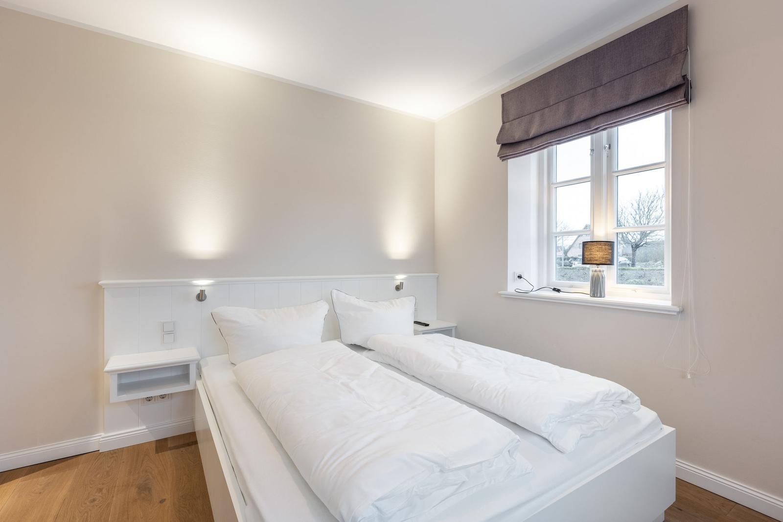 Schlafzimmer mit weißem Bett, Fenster und Nachttisch.