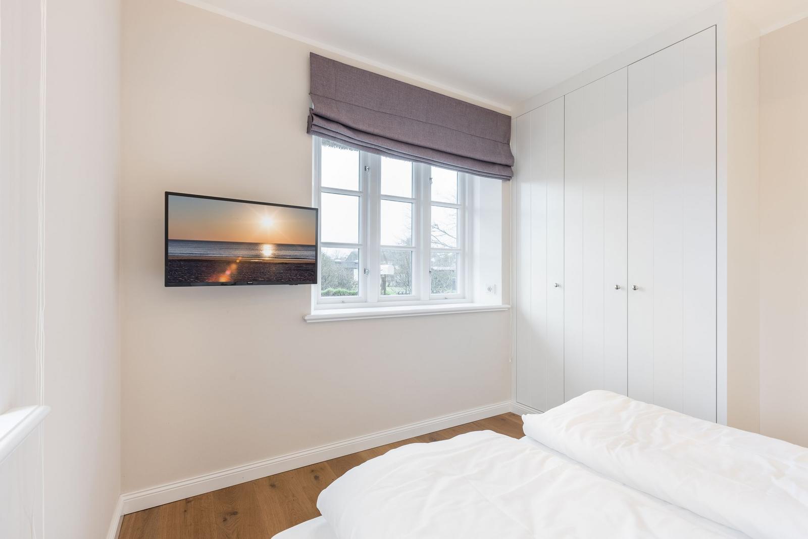 Schlafzimmer mit Bett, Fenster und TV an der Wand.