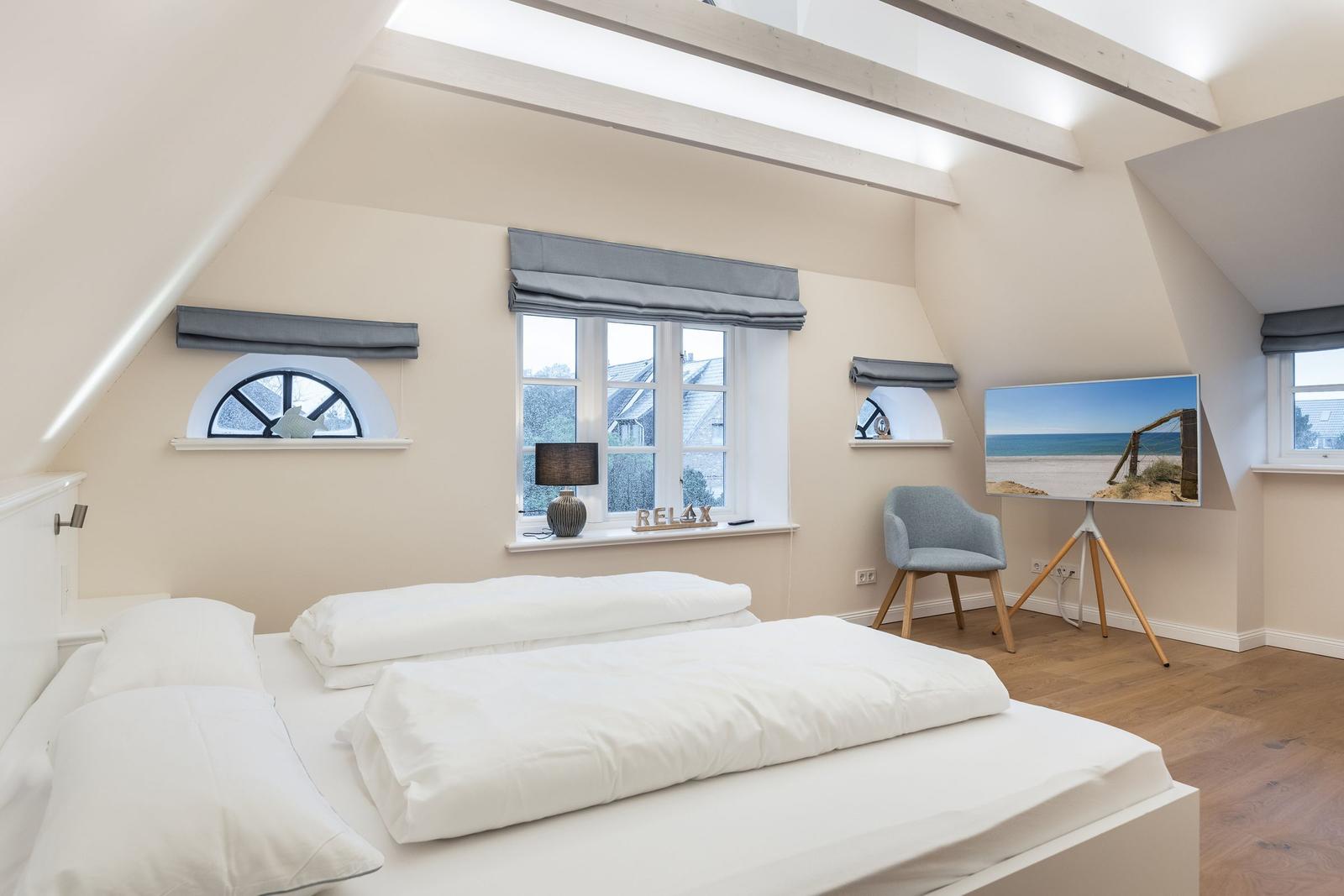 Schlafzimmer mit Dachschrägen, großem Bett und Fenstern mit Blick nach außen.