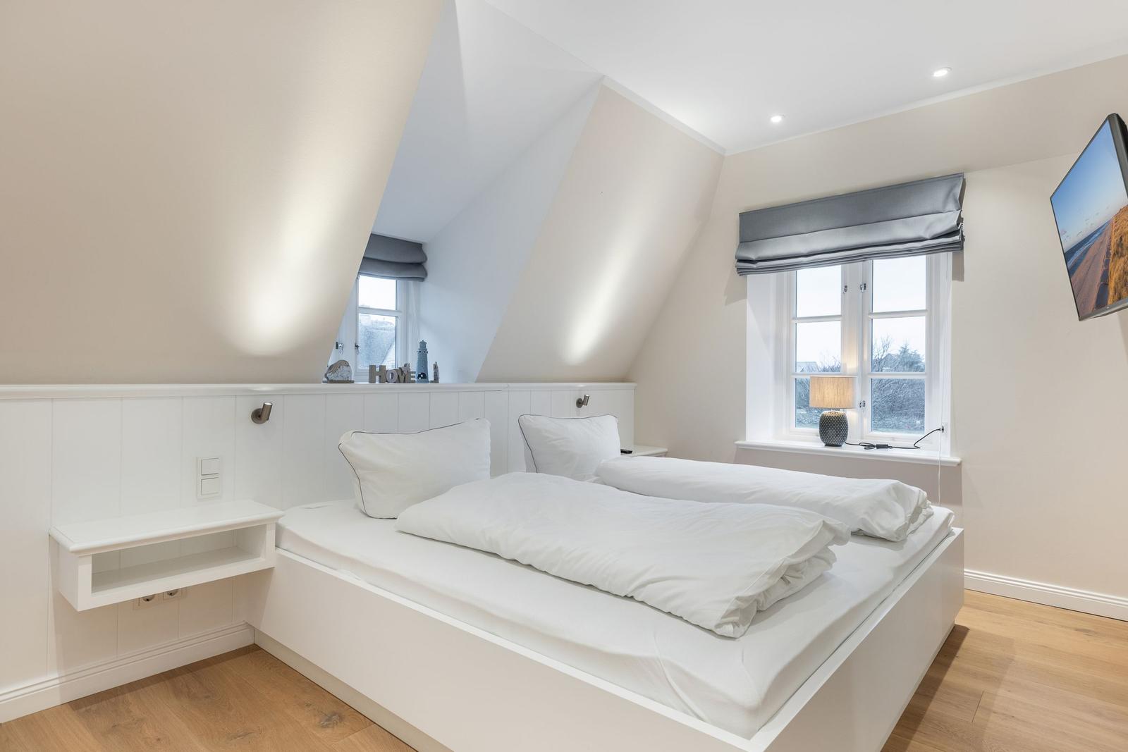 Schlafzimmer mit Doppelbett, Fenster und TV. Holzboden und weiße Wände.