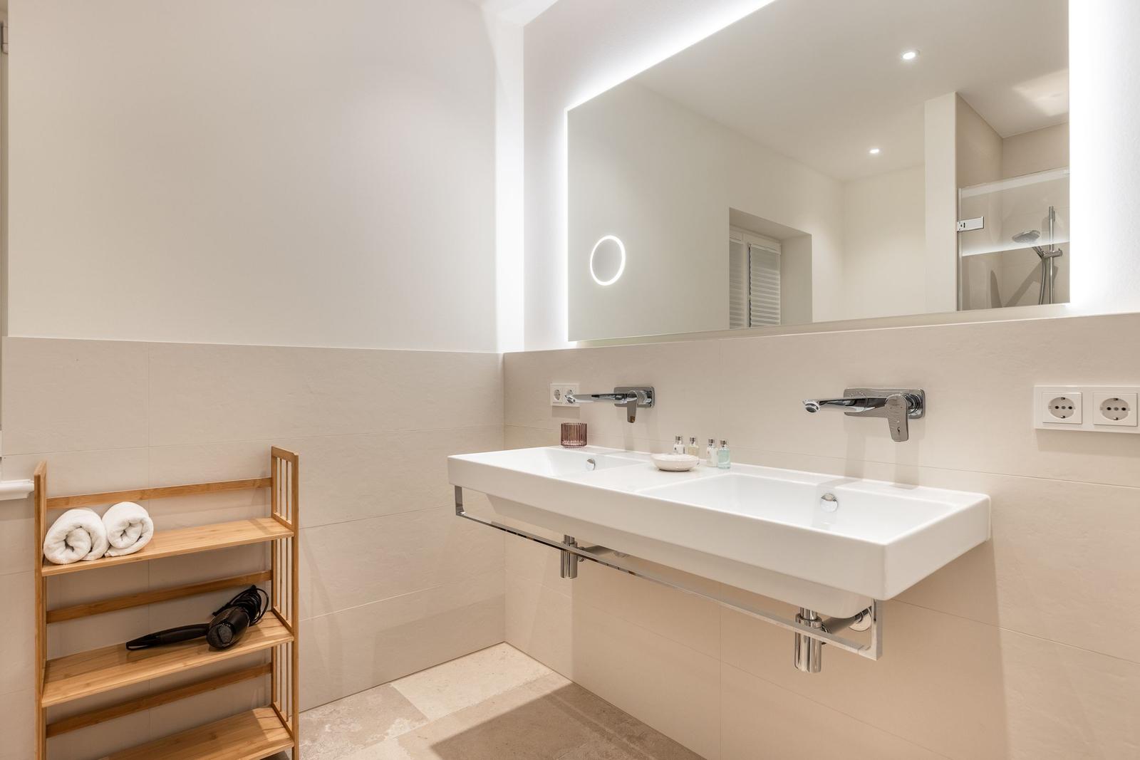 Badezimmer mit Waschbecken, Spiegel und Holzregal mit Handtüchern.