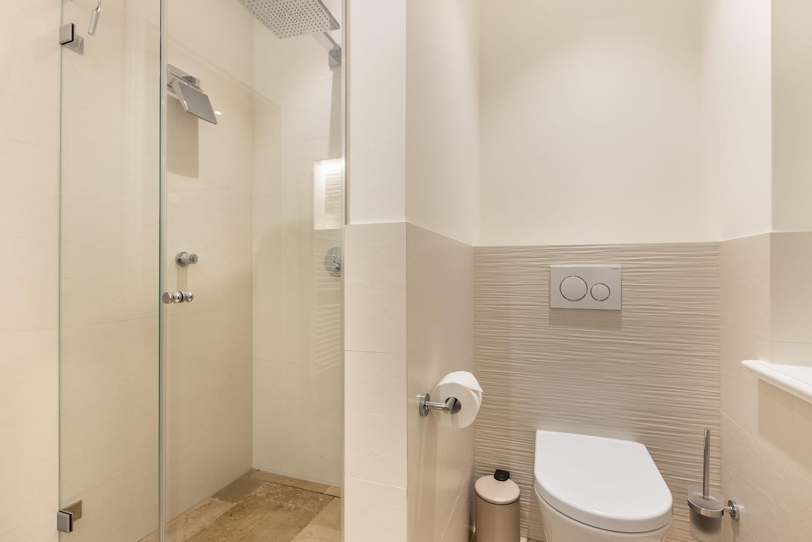 Dusche mit Glaswand, Toilette und Toilettenpapierhalter.