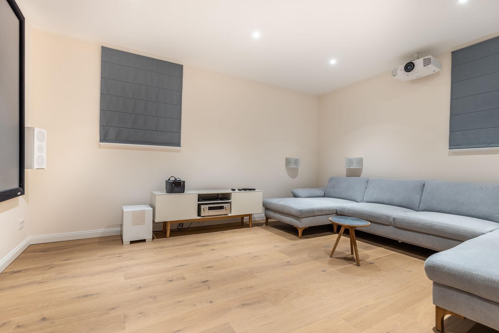 Wohnzimmer mit grauem Sofa, Holzboden und Projektionssystem.