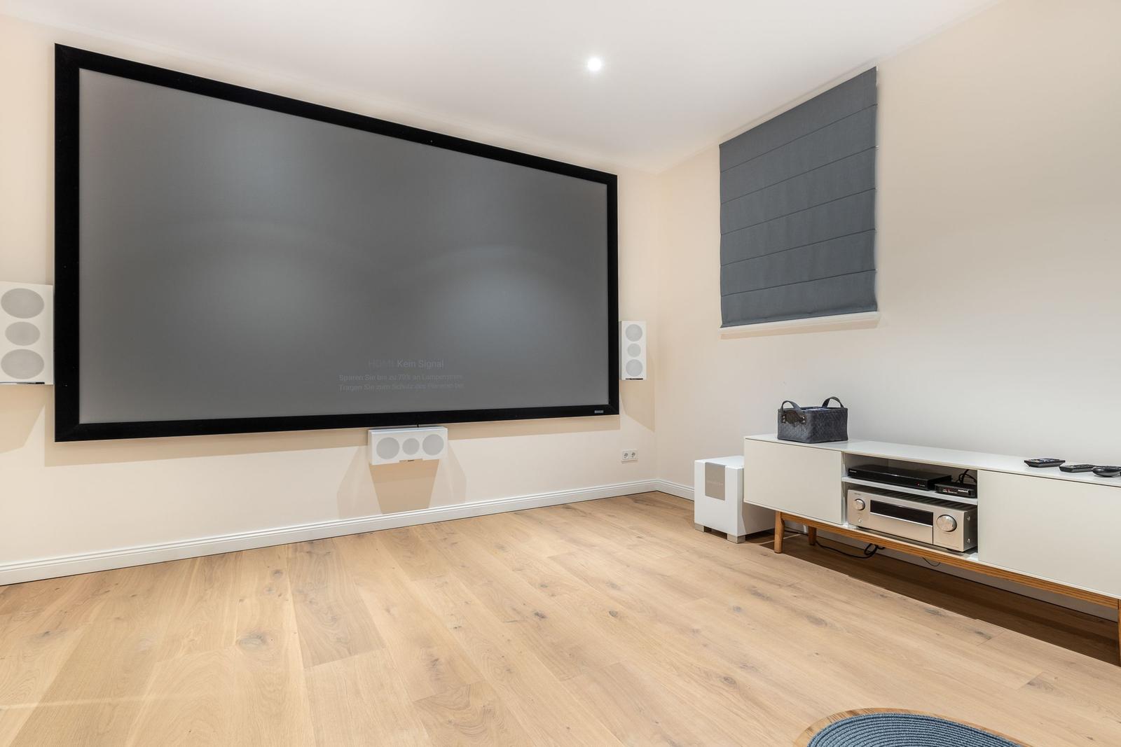 Großer Home Cinema Raum mit Projektionswand und modernem Audio-Setup.