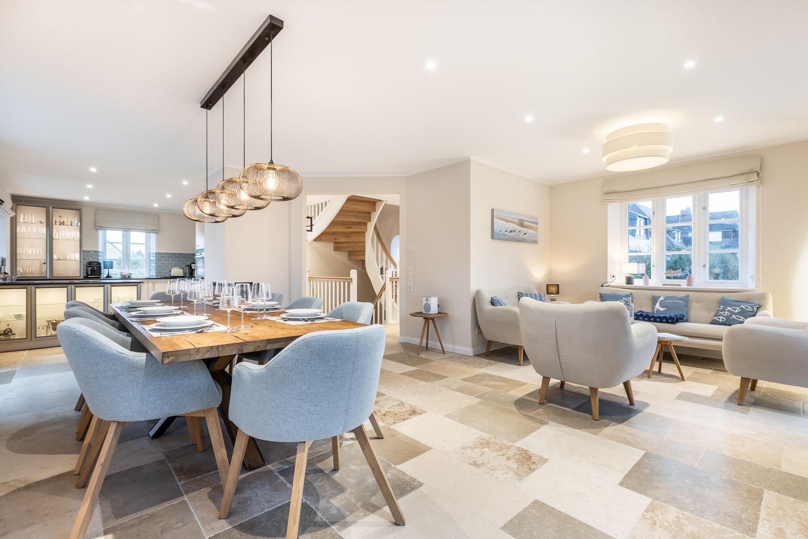 Essbereich mit Holztisch und Stühlen, Wohnbereich mit Sofa und Sesseln, Flur mit Treppe.