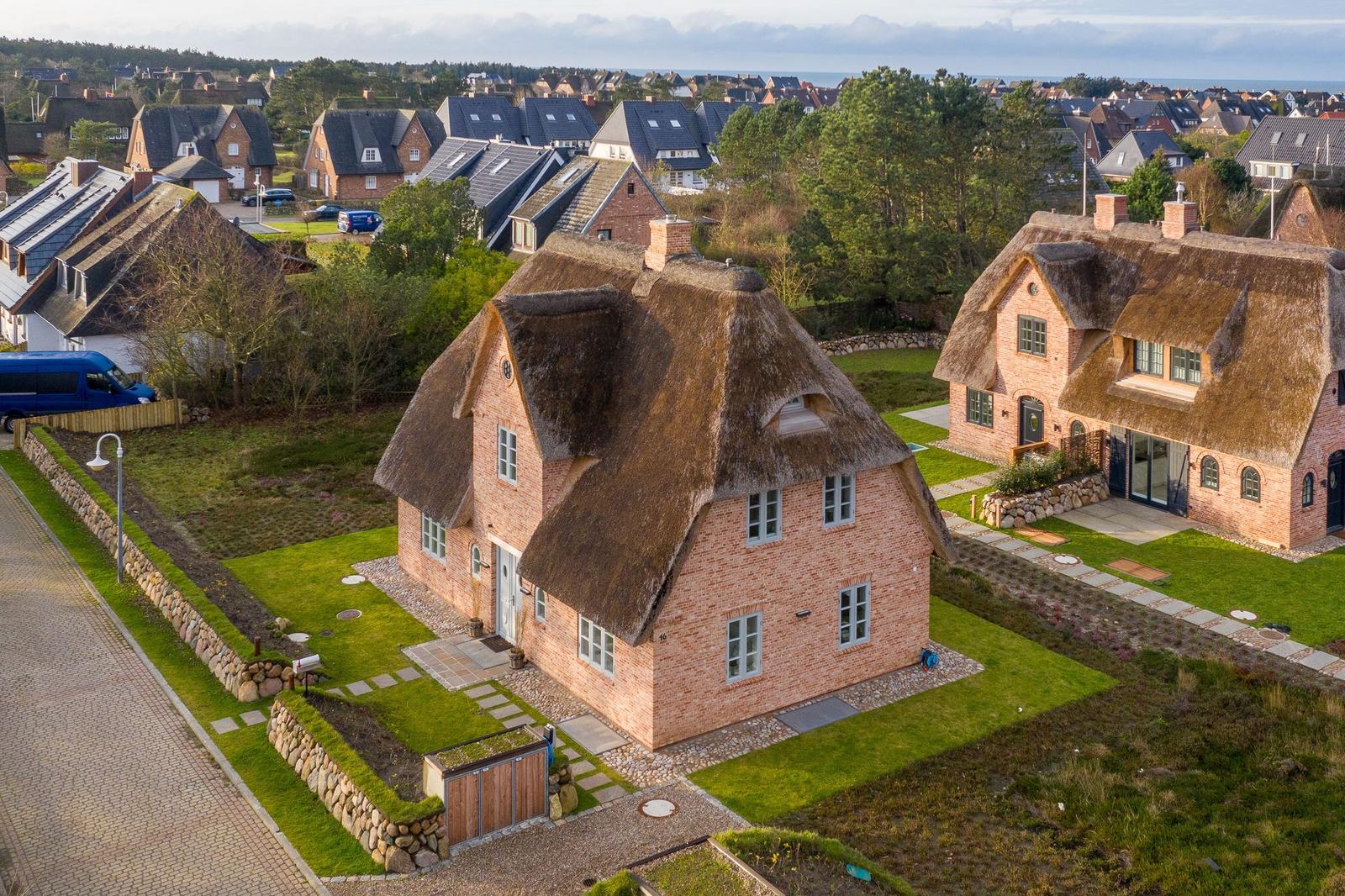 Dorfhaus mit Strohdach und Steinmauern. Grünflächen und Nebengebäude im Hintergrund.