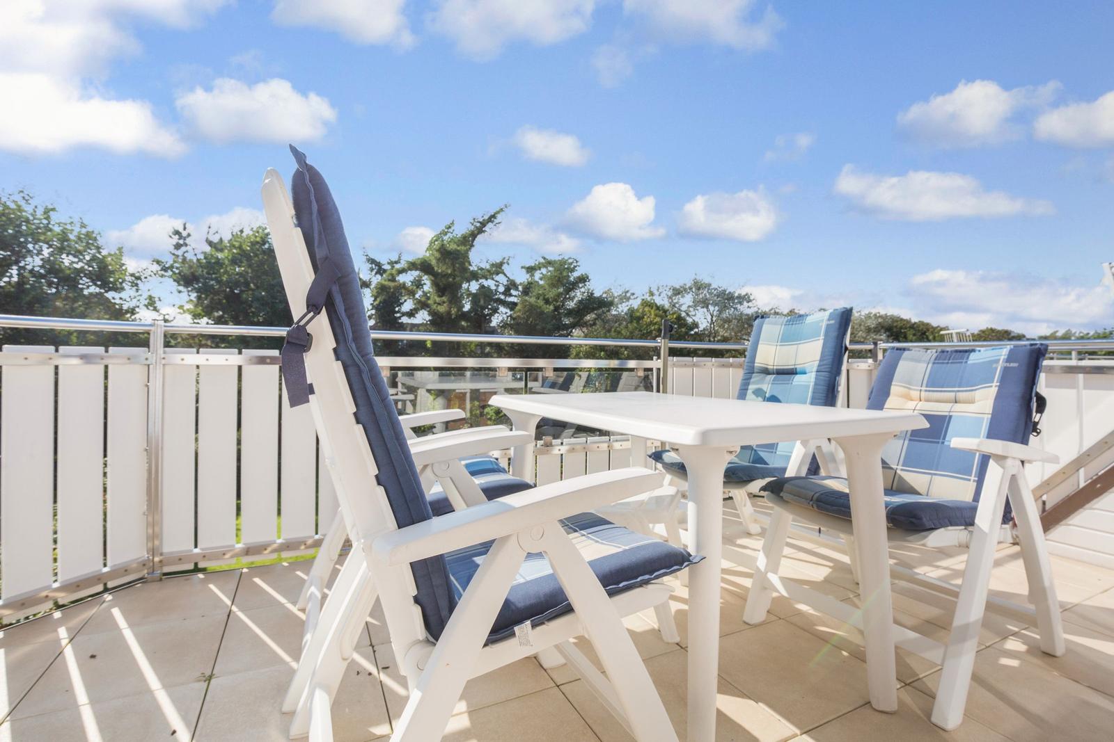 Terrace with white chairs and table under blue sky.