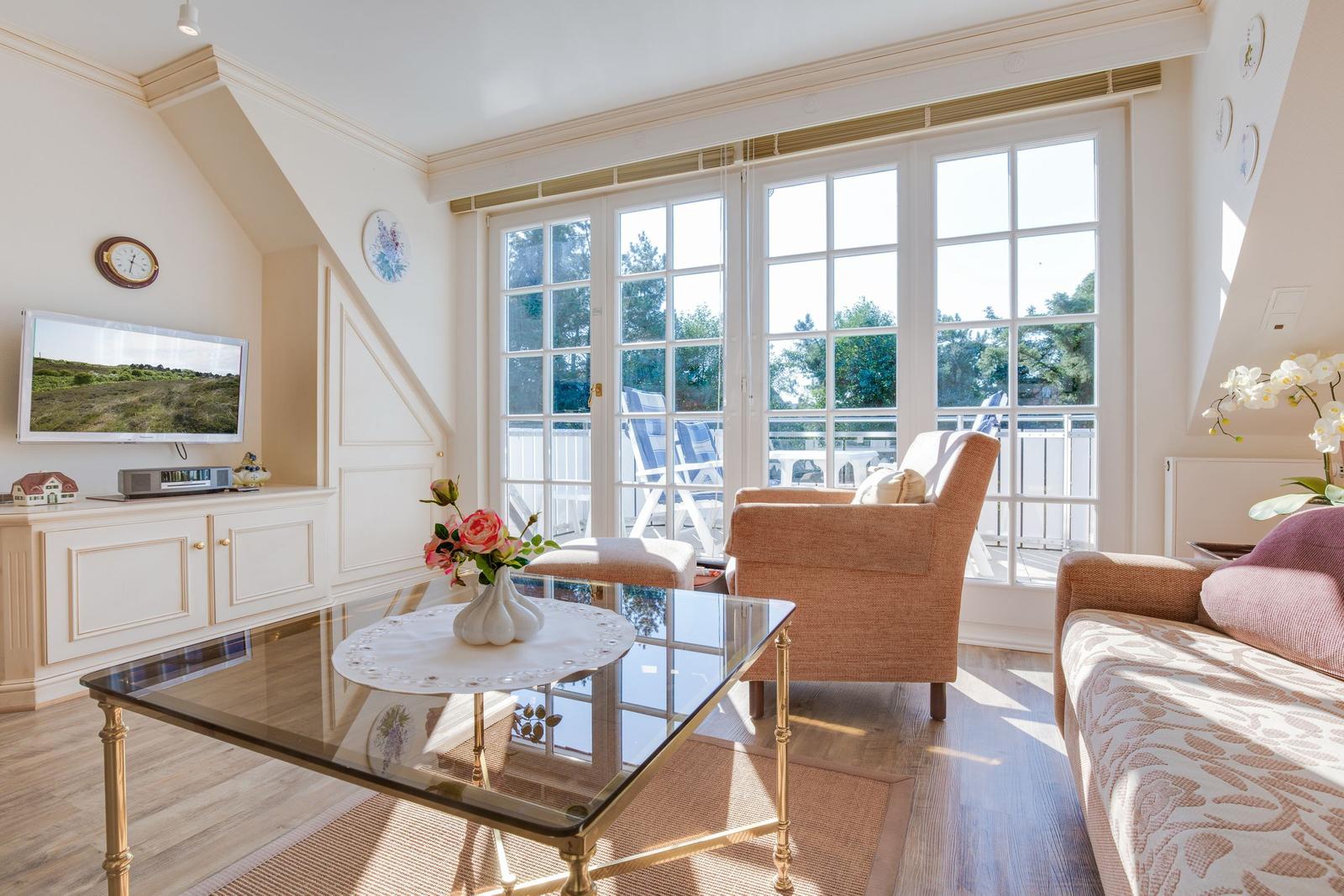 Living room with glass table, sofa, and armchair. Large window front with balcony view.