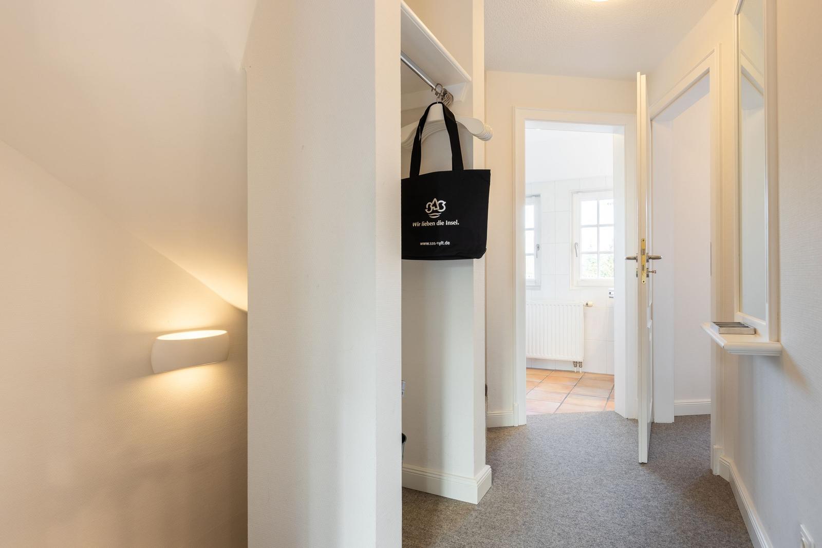 Hallway with clothes rack, wall lamp, and view into bathroom.