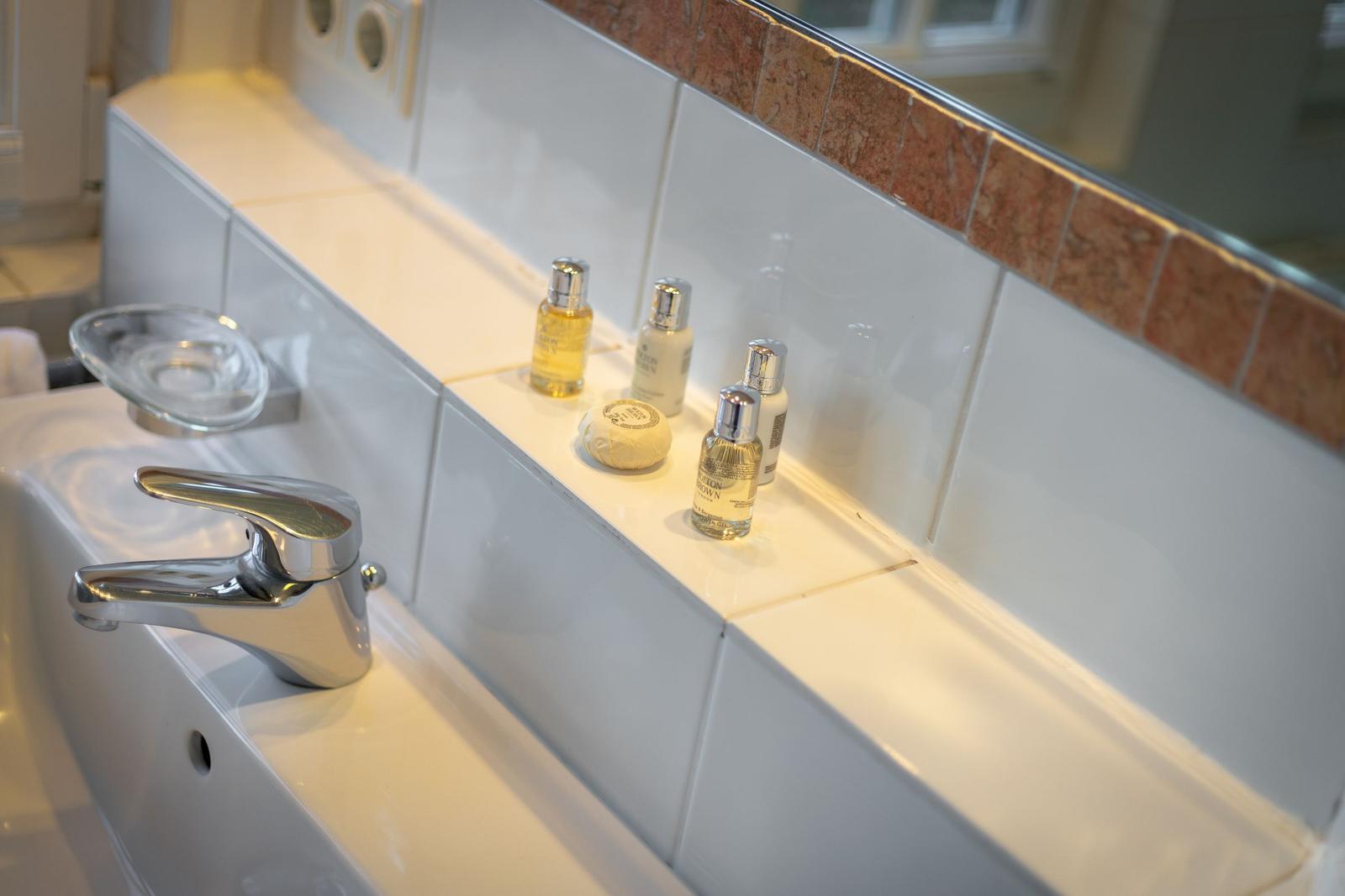 Sink with faucet and toiletries on white tiled wall.