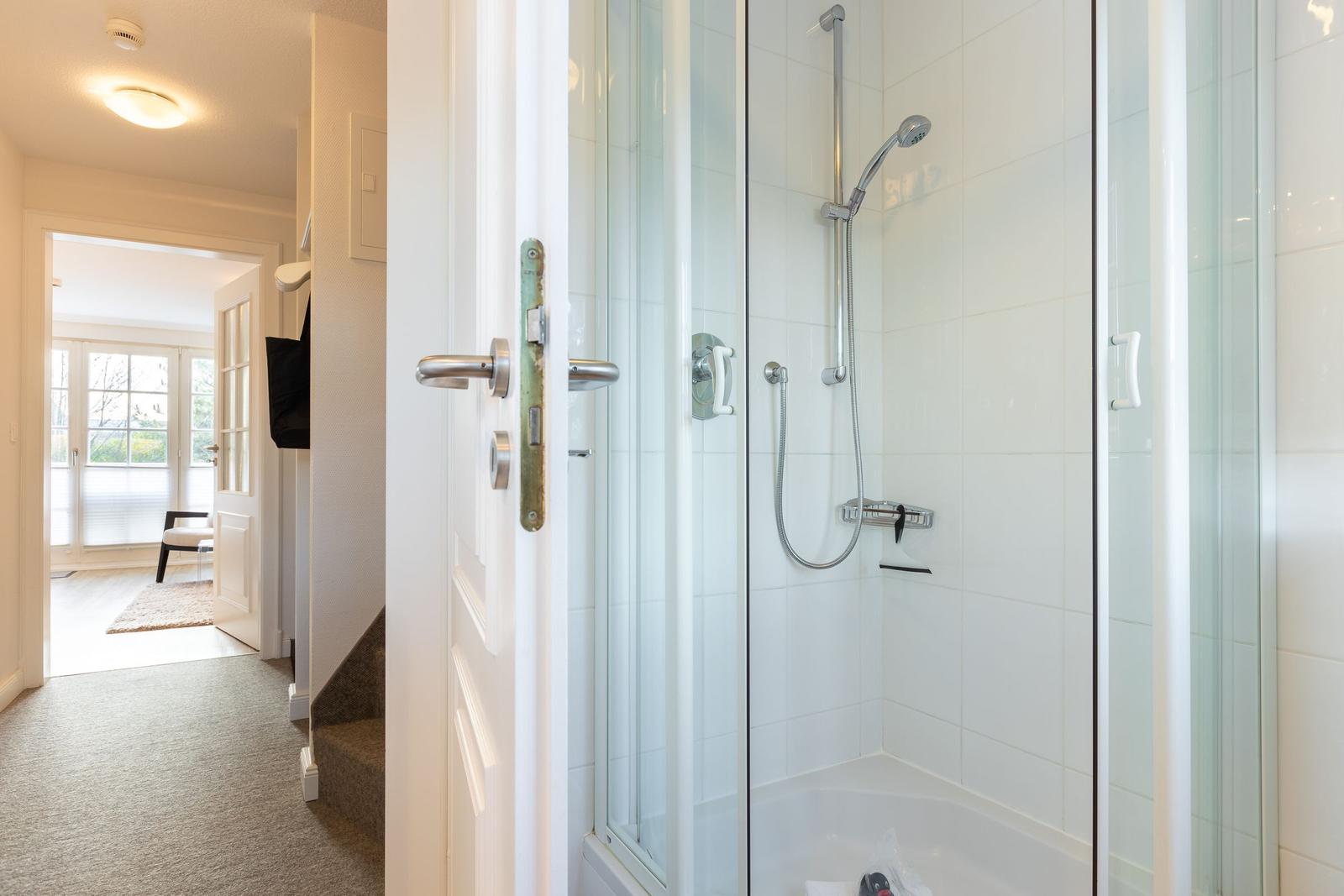 Shower cabin with glass enclosure and shower head. Door leads to living area with window.