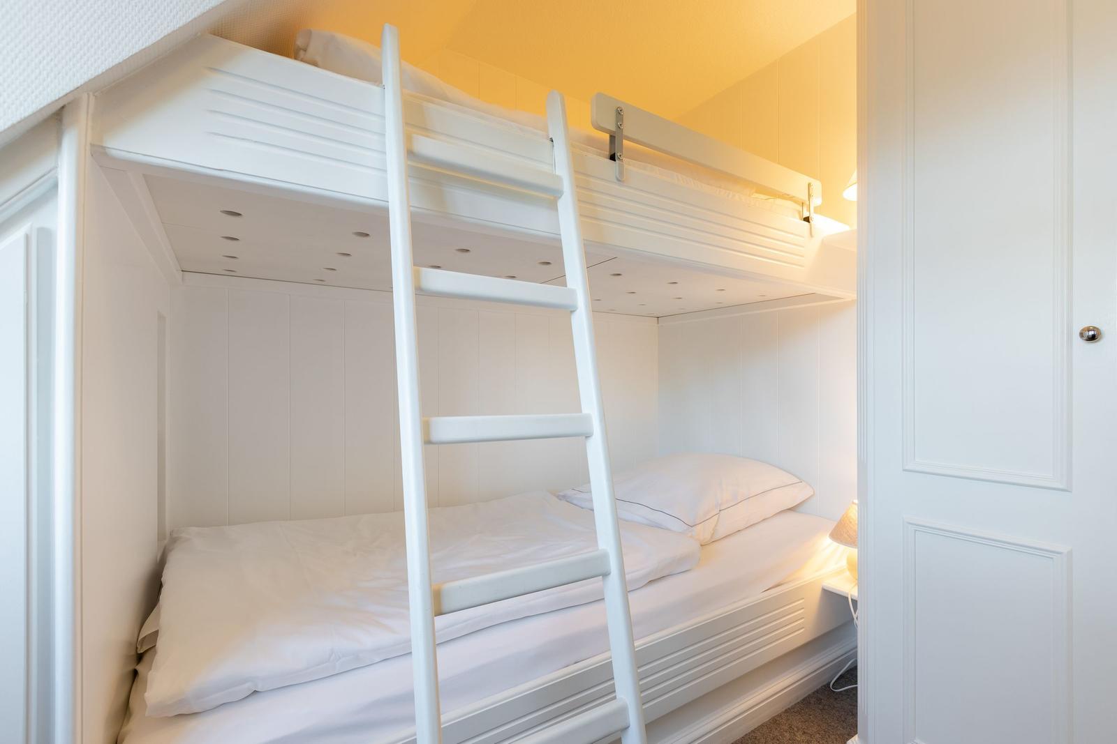 A bedroom with two white bunk beds and a ladder.
